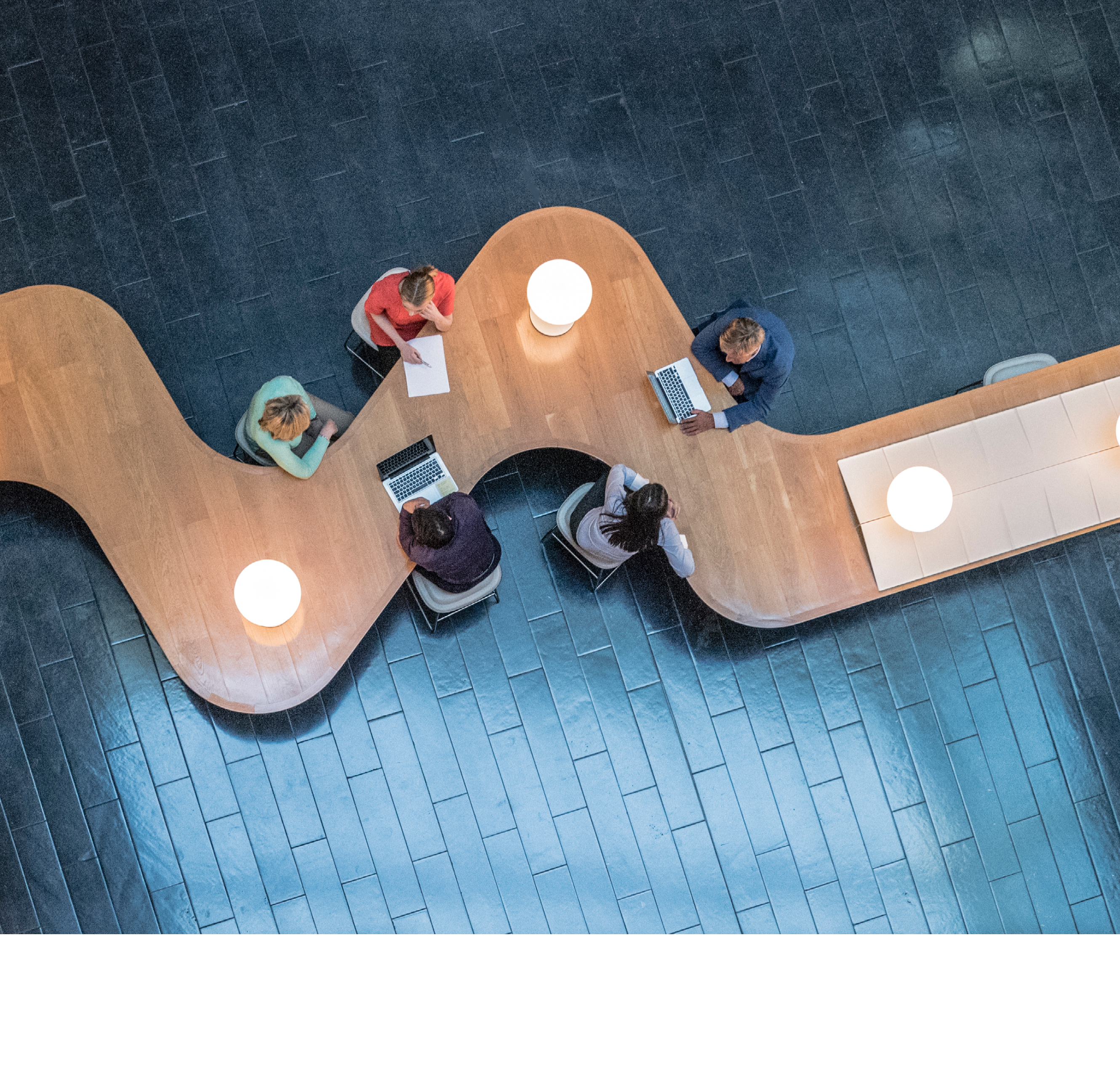 Panoramic overhead view of several business meetings going on in the communal area of a modern office building.