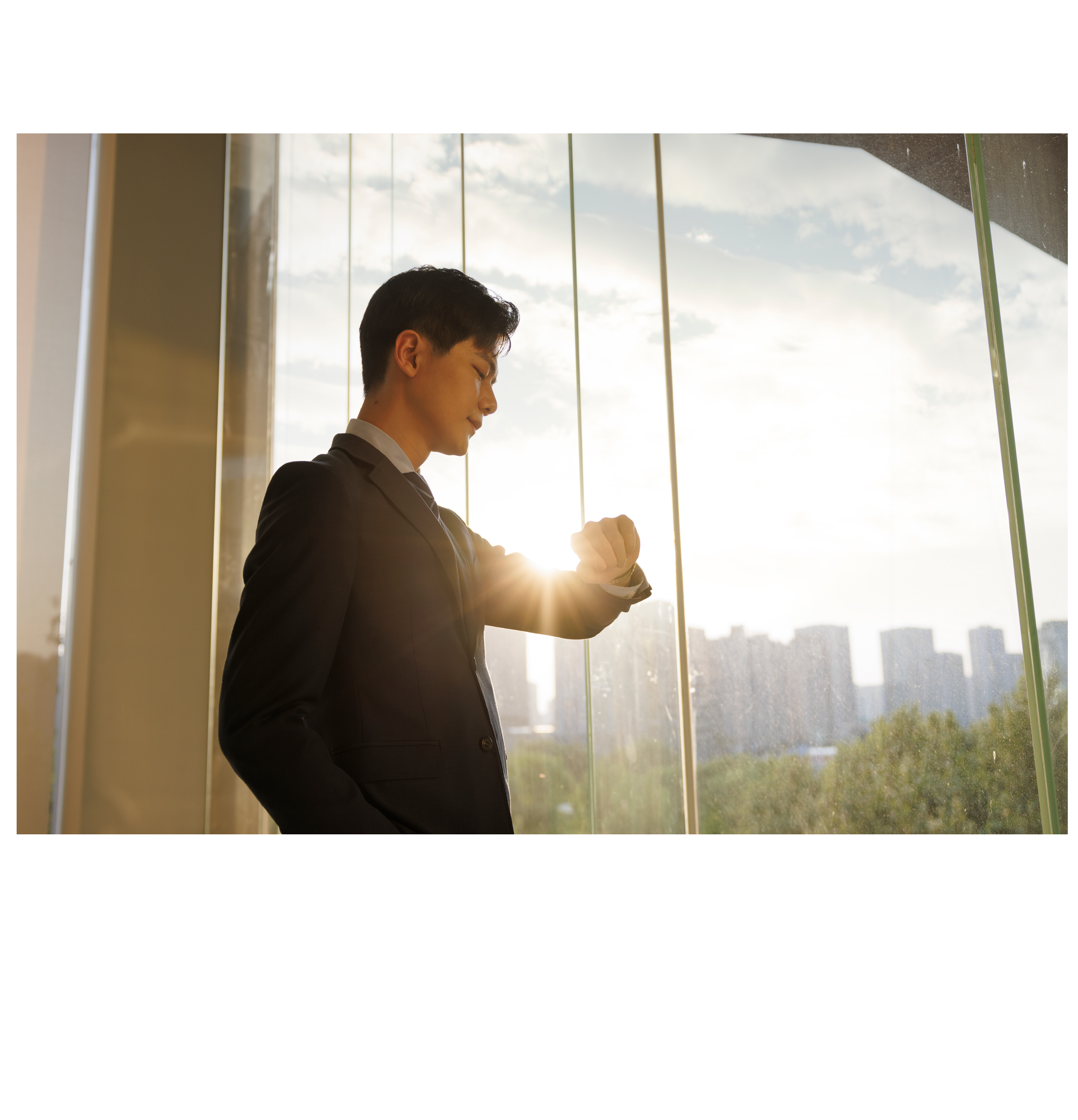 A young asian businessman, dressed in a gray suit, looked at his watch in front of the office window