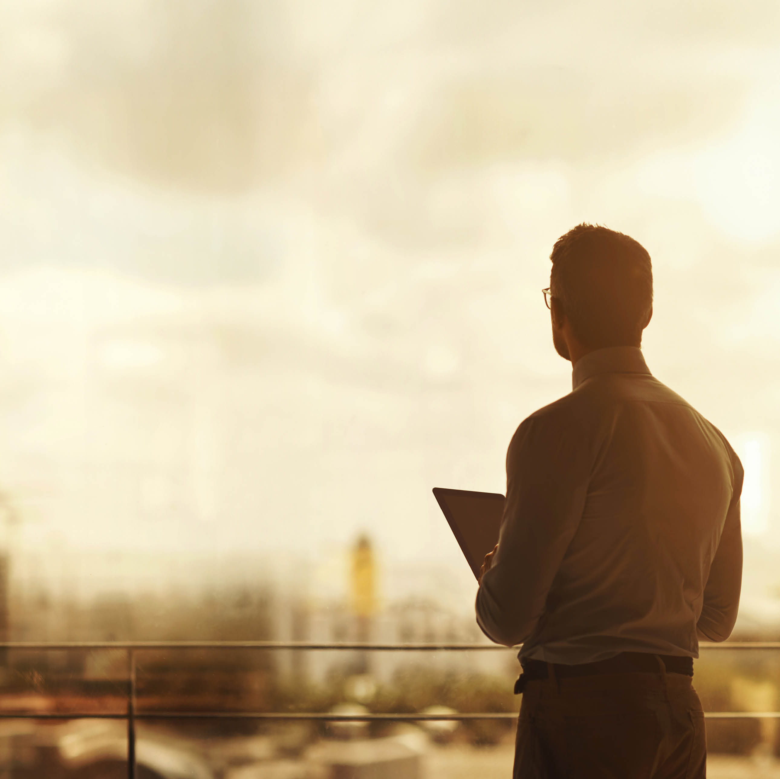 Silhouette of a mature businessman standing in front of an office window and using a digital tablet