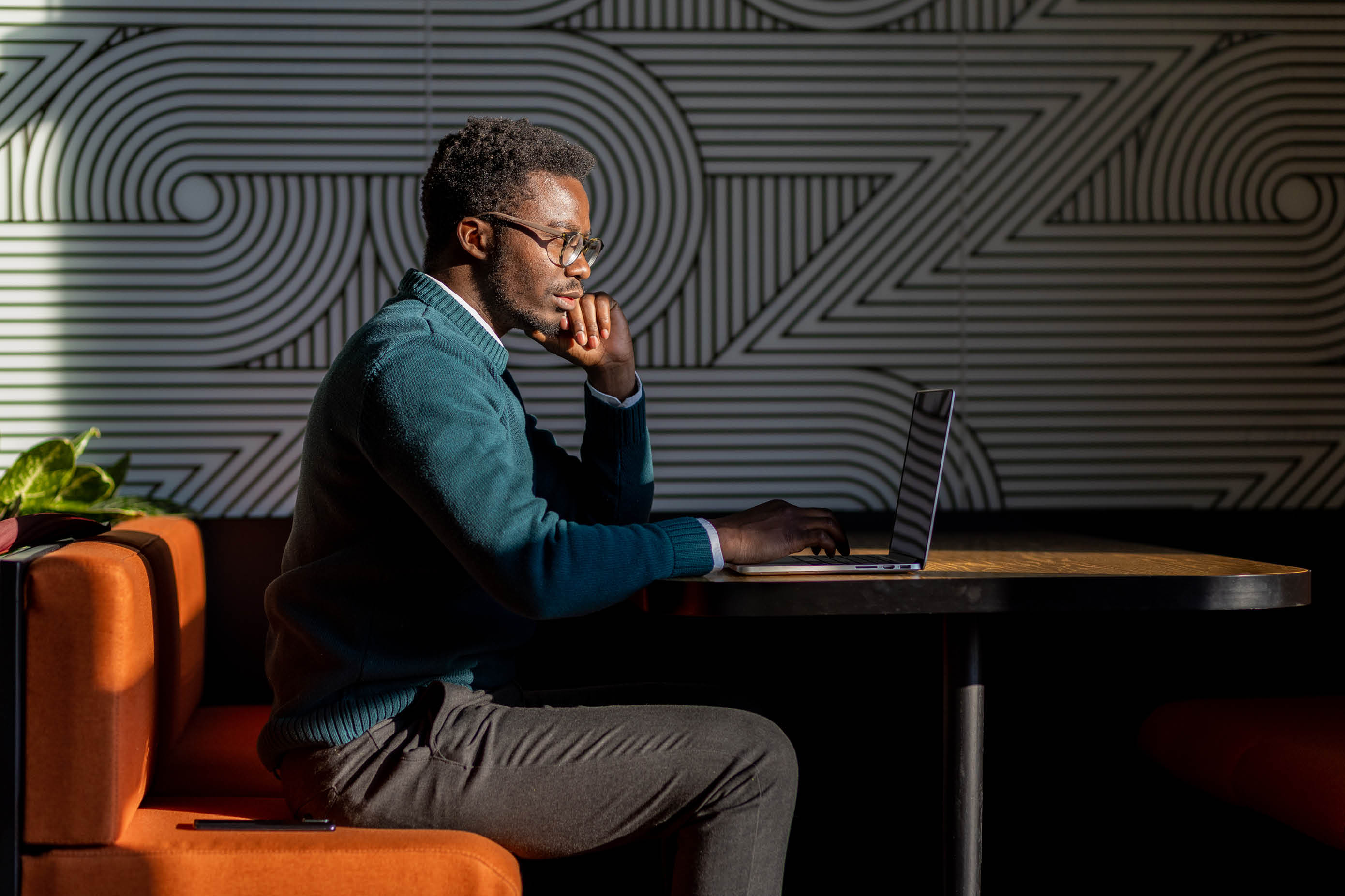 Young black businessman in a coworking space, new office, modern environment. Young African-American freelancer working on his laptop in a beautifully sunlit space.