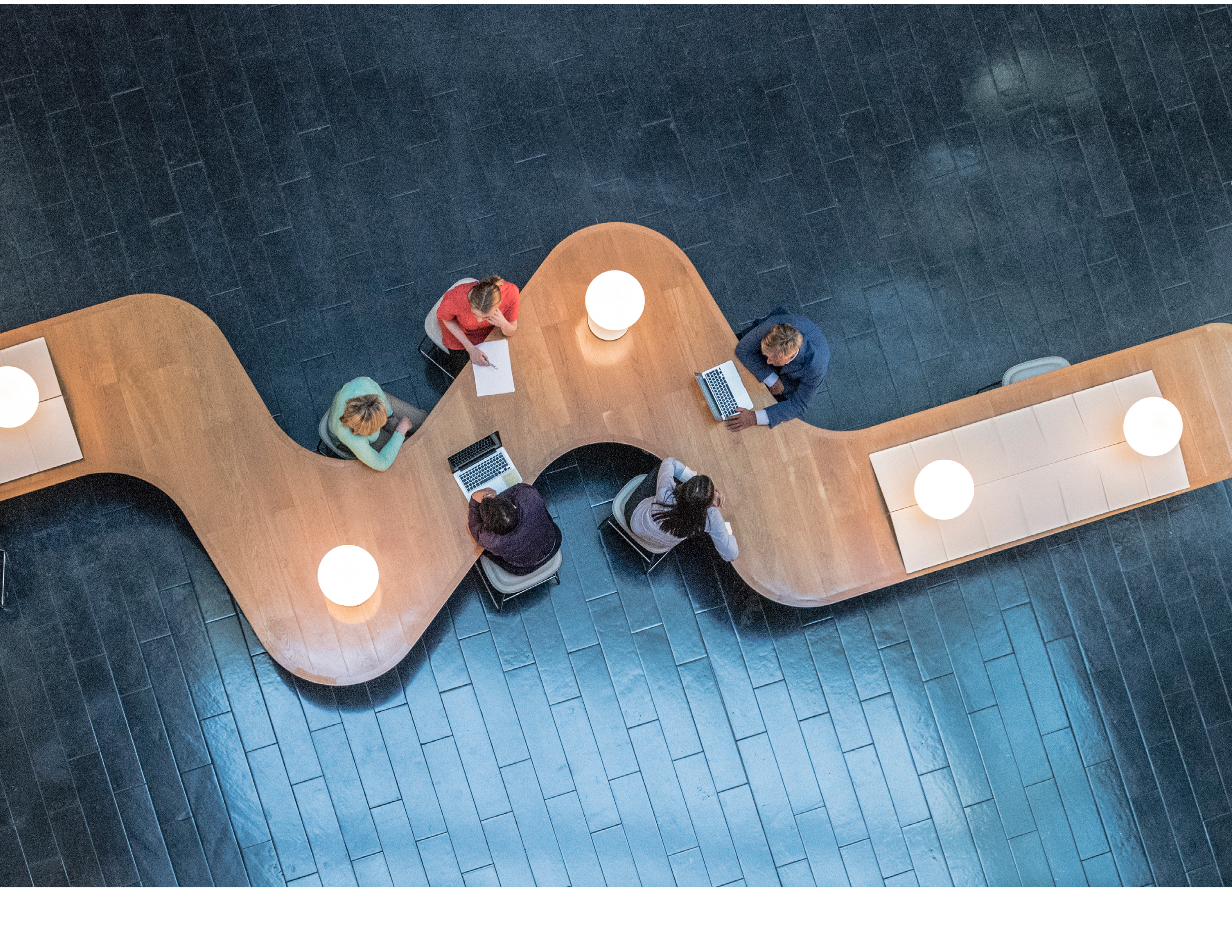 Panoramic overhead view of several business meetings going on in the communal area of a modern office building.