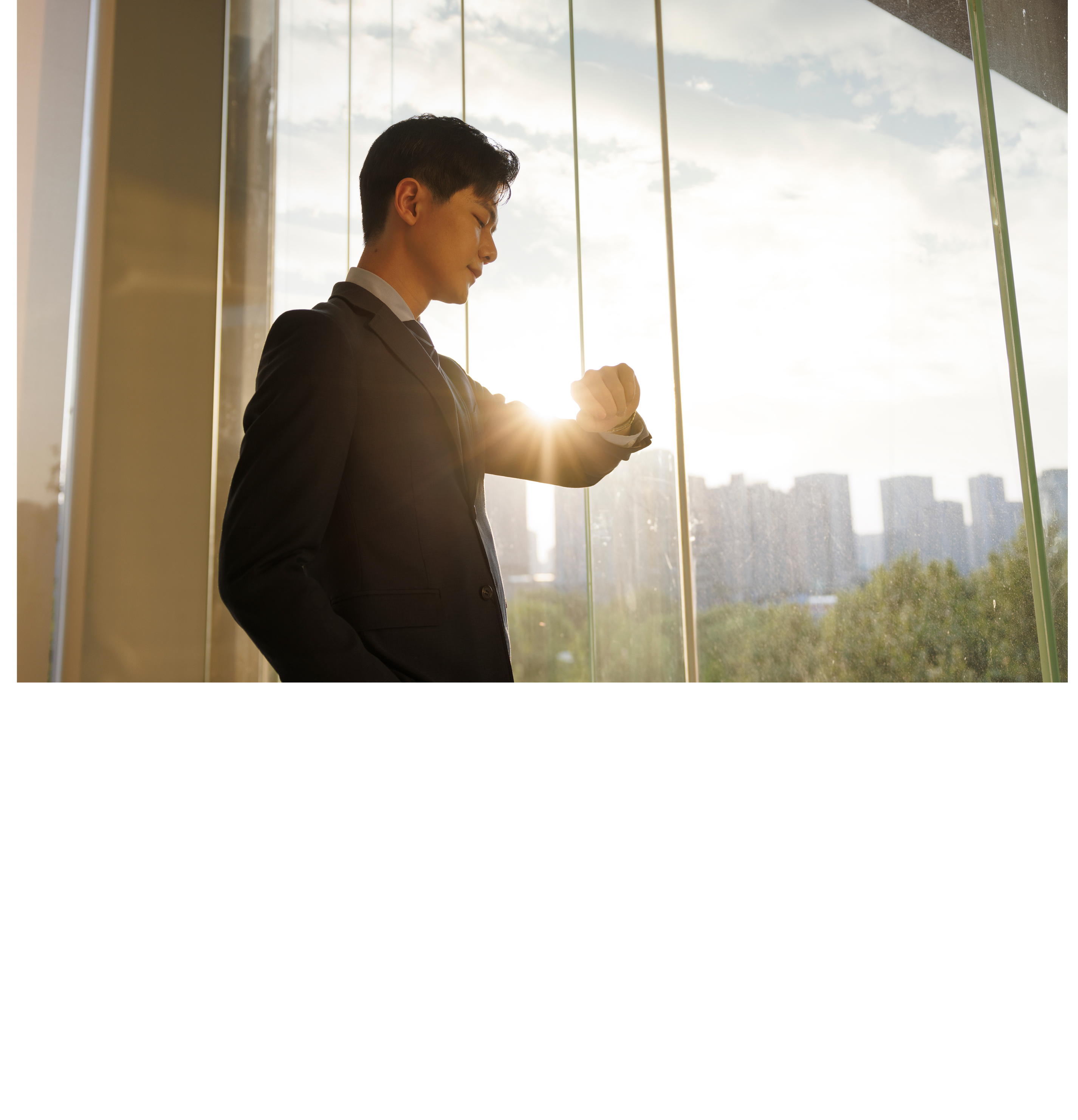 A young asian businessman, dressed in a gray suit, looked at his watch in front of the office window