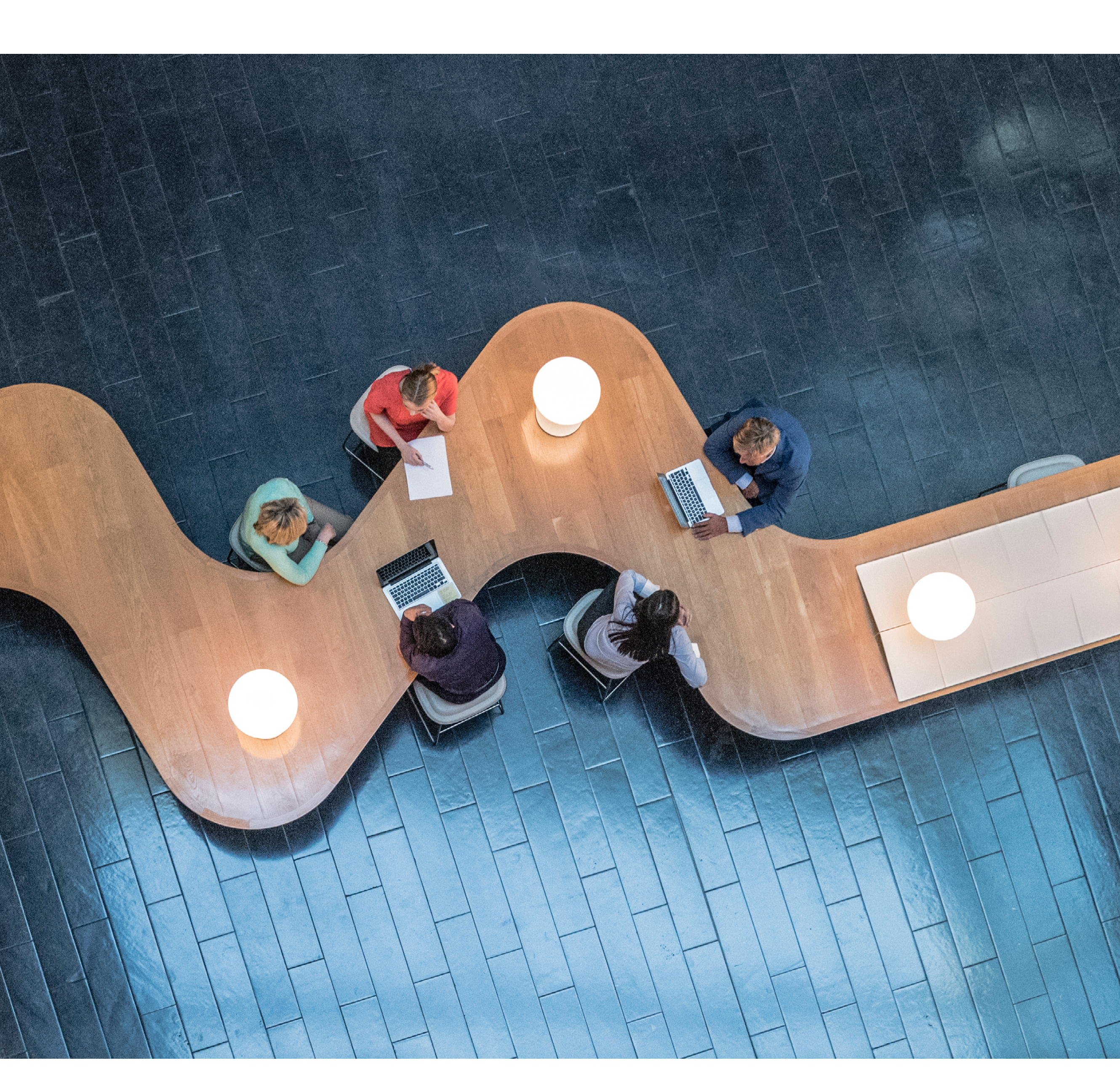 Panoramic overhead view of several business meetings going on in the communal area of a modern office building.