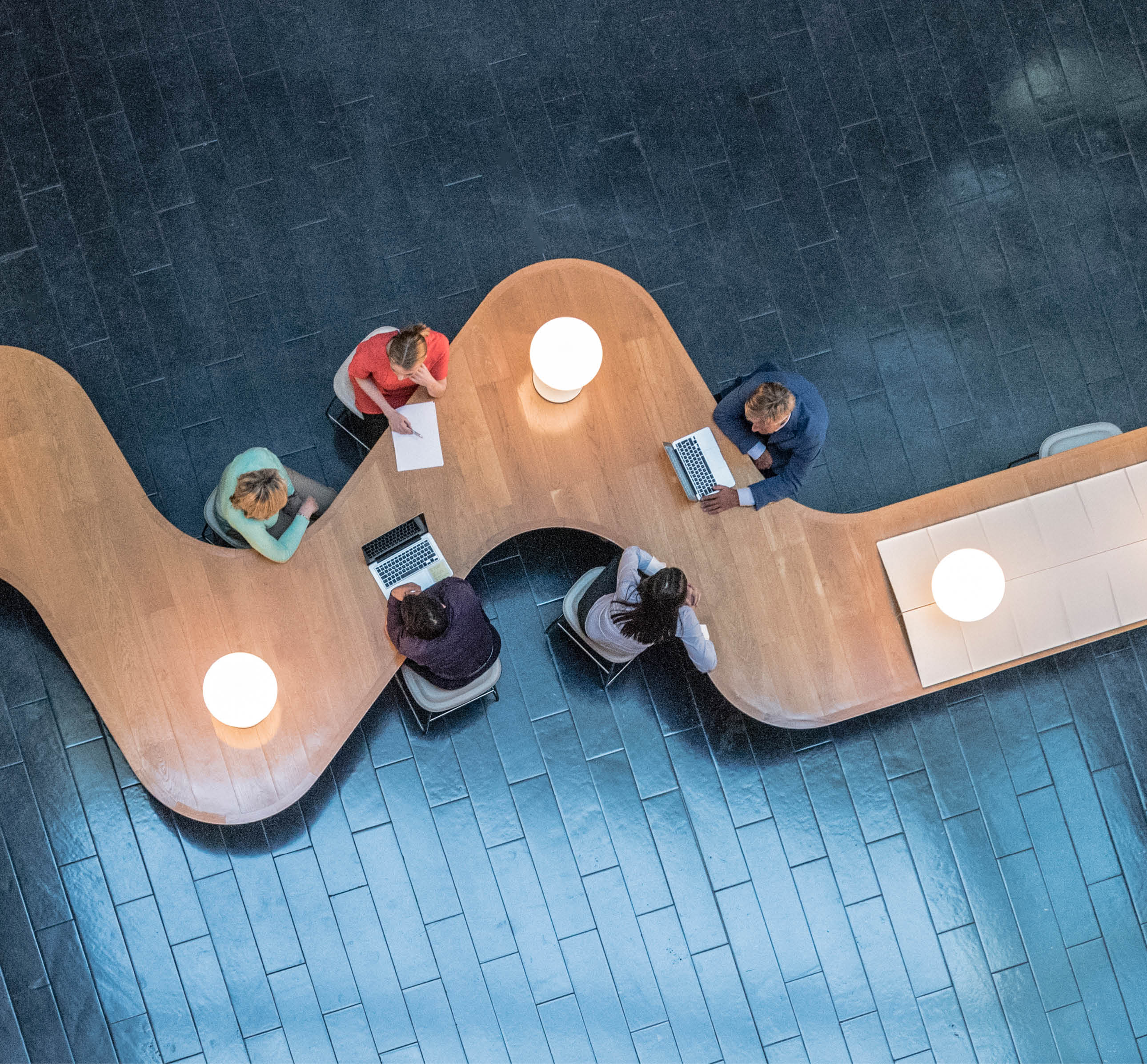 Panoramic overhead view of several business meetings going on in the communal area of a modern office building.