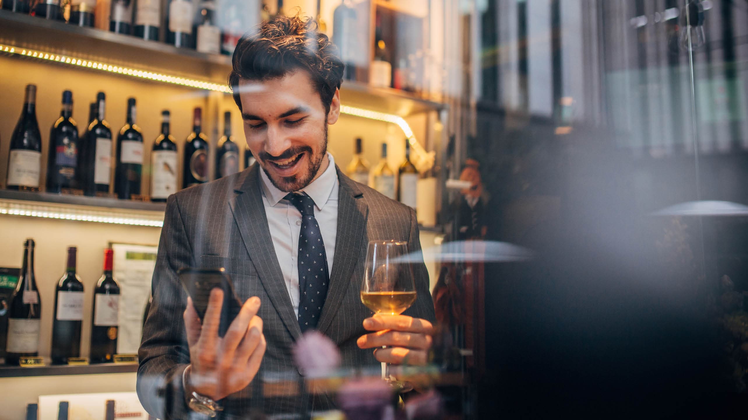 One handsome businessman in a suit drinking white wine and text messaging 