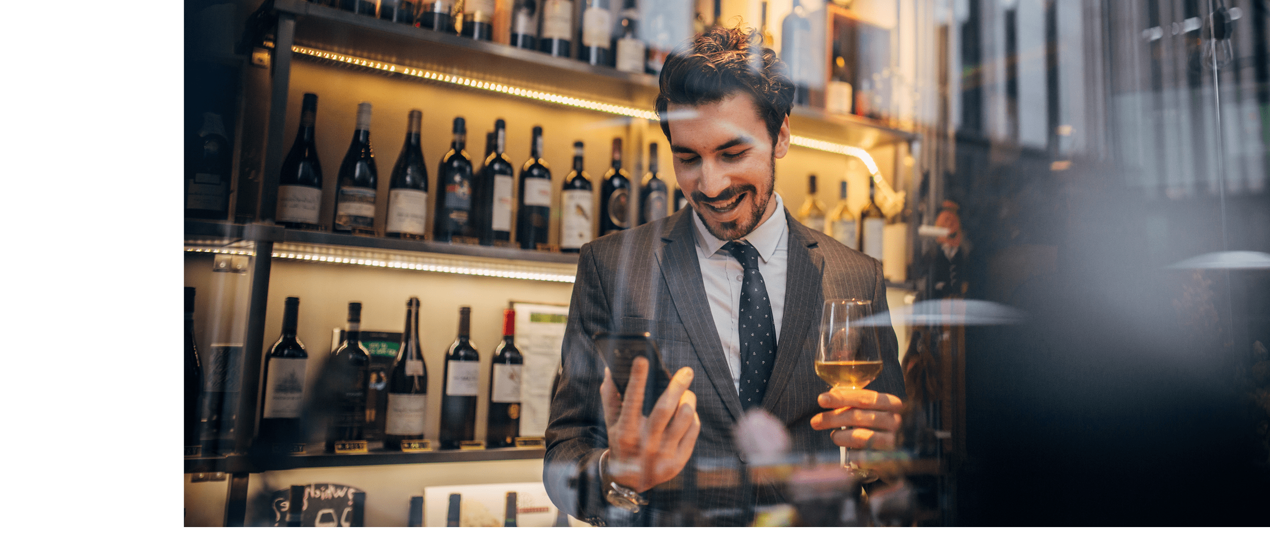 One handsome businessman in a suit drinking white wine and text messaging 