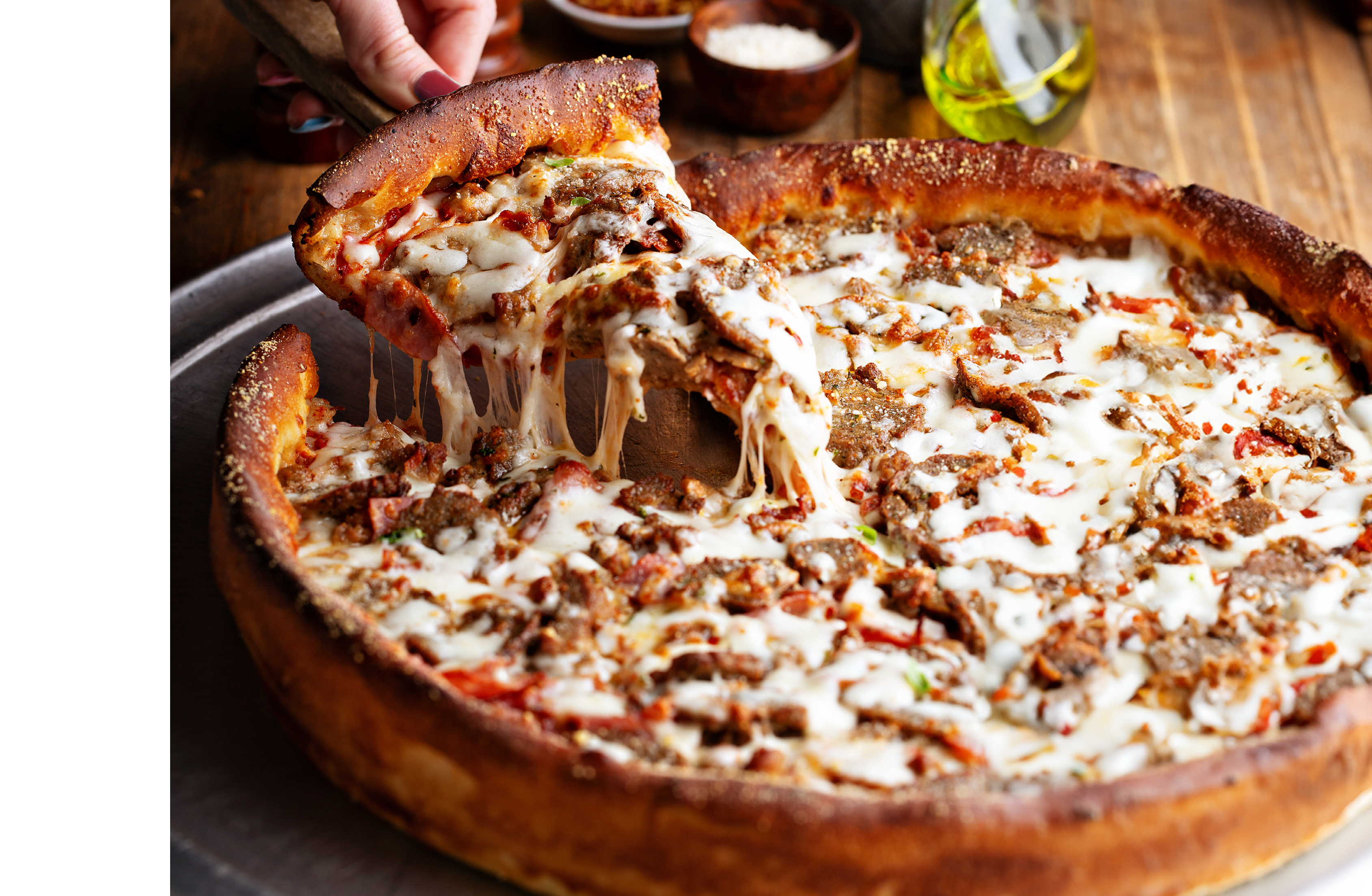 Deep dish meat pizza on a wooden table with a slice being pulled
