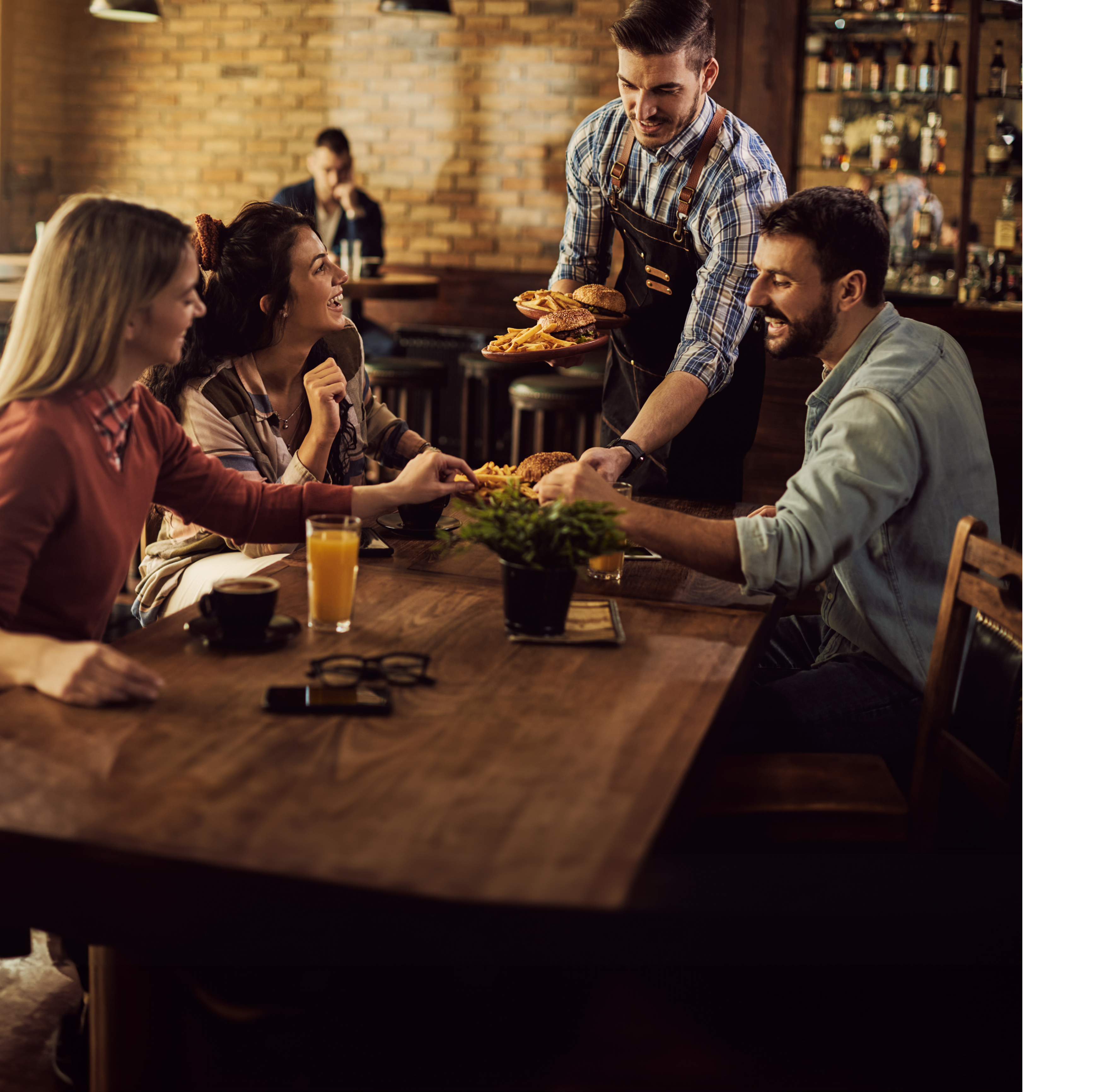 Group of happy friends having fun while waiter is serving them food in a pub.