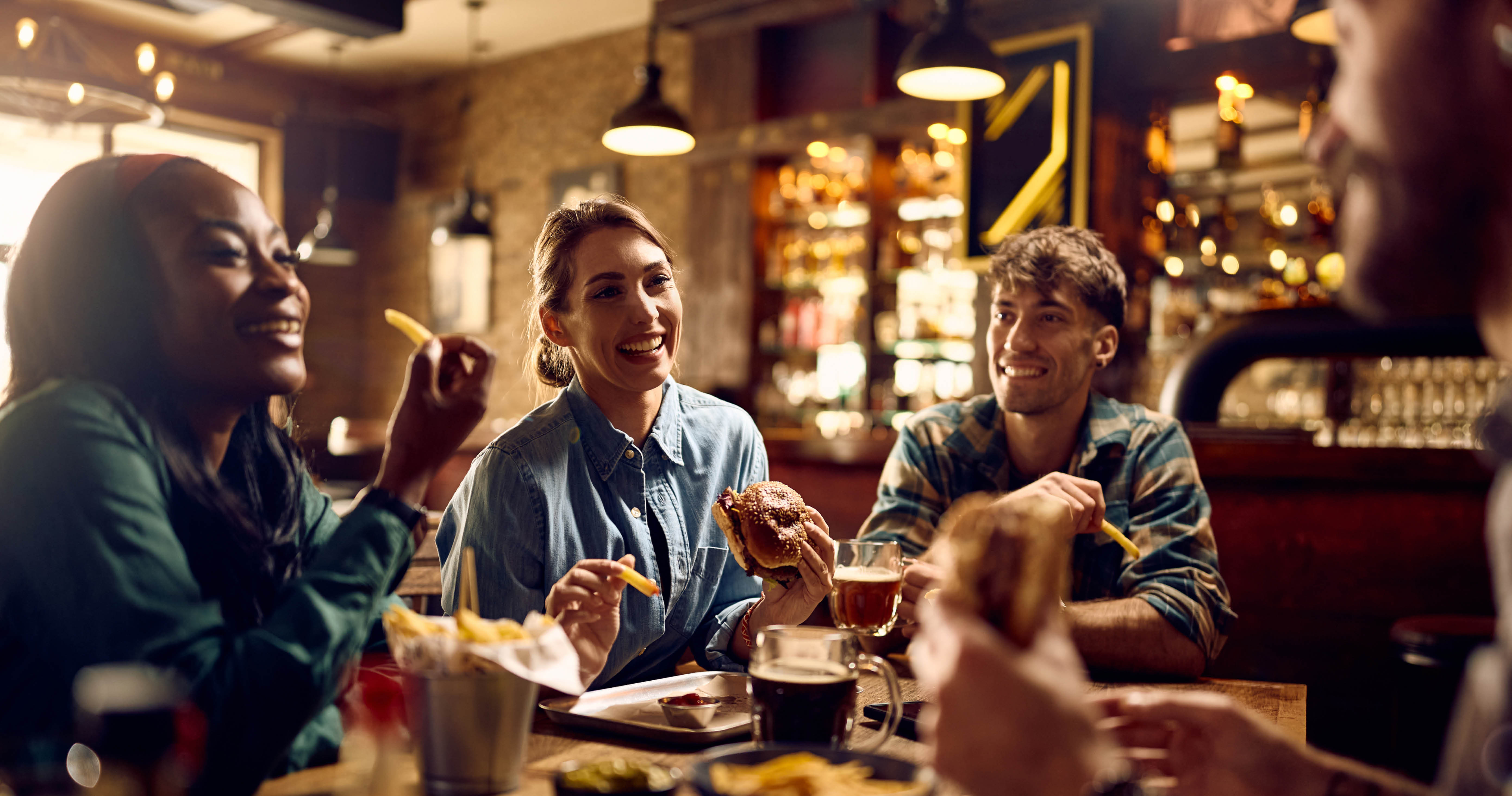 Young happy woman and her friends talking while eating in a pub.