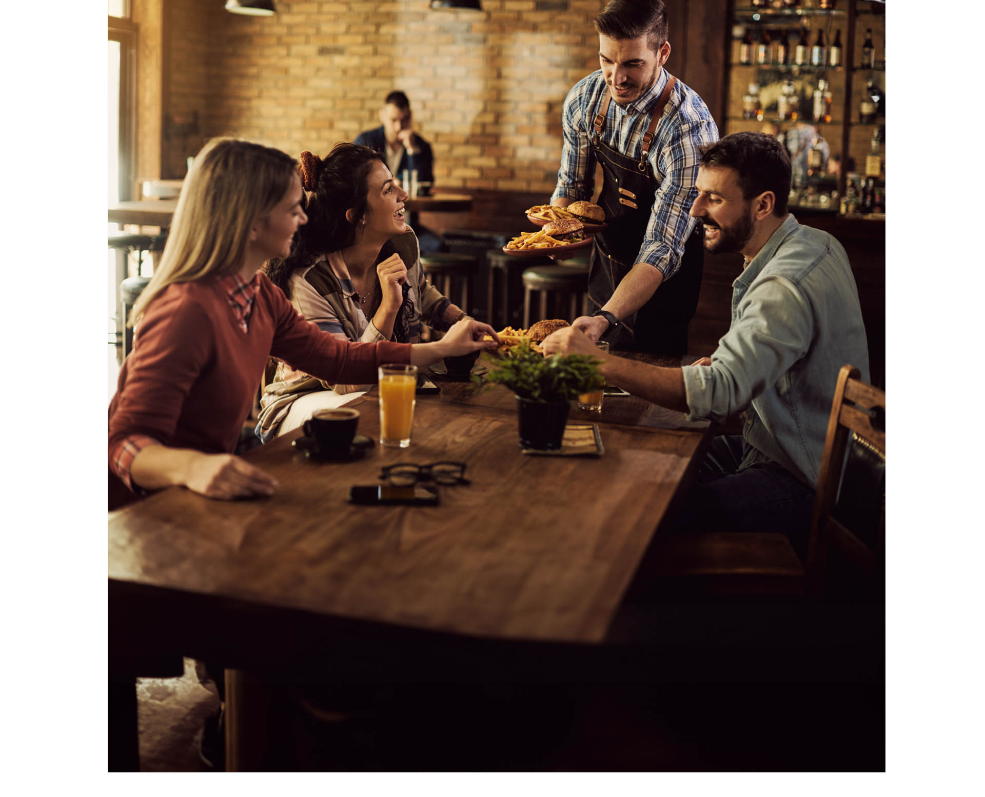 Group of happy friends having fun while waiter is serving them food in a pub.