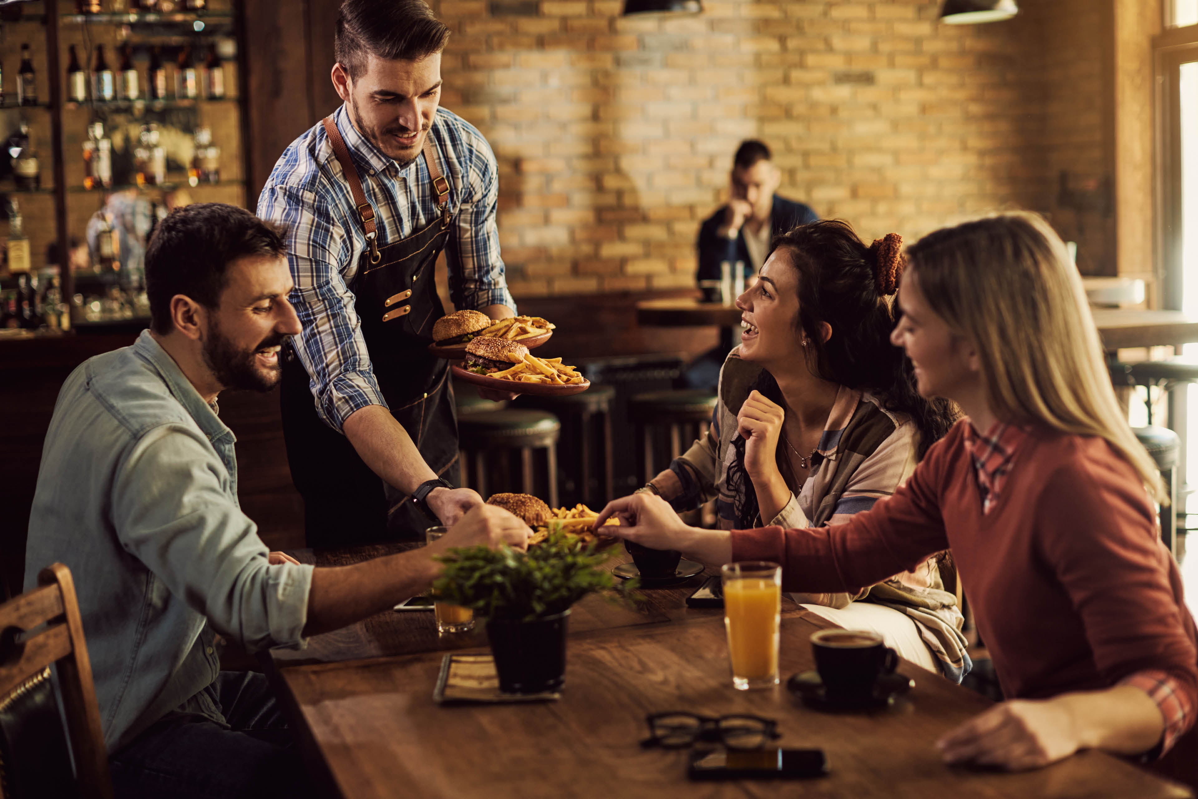 Group of happy friends having fun while waiter is serving them food in a pub.