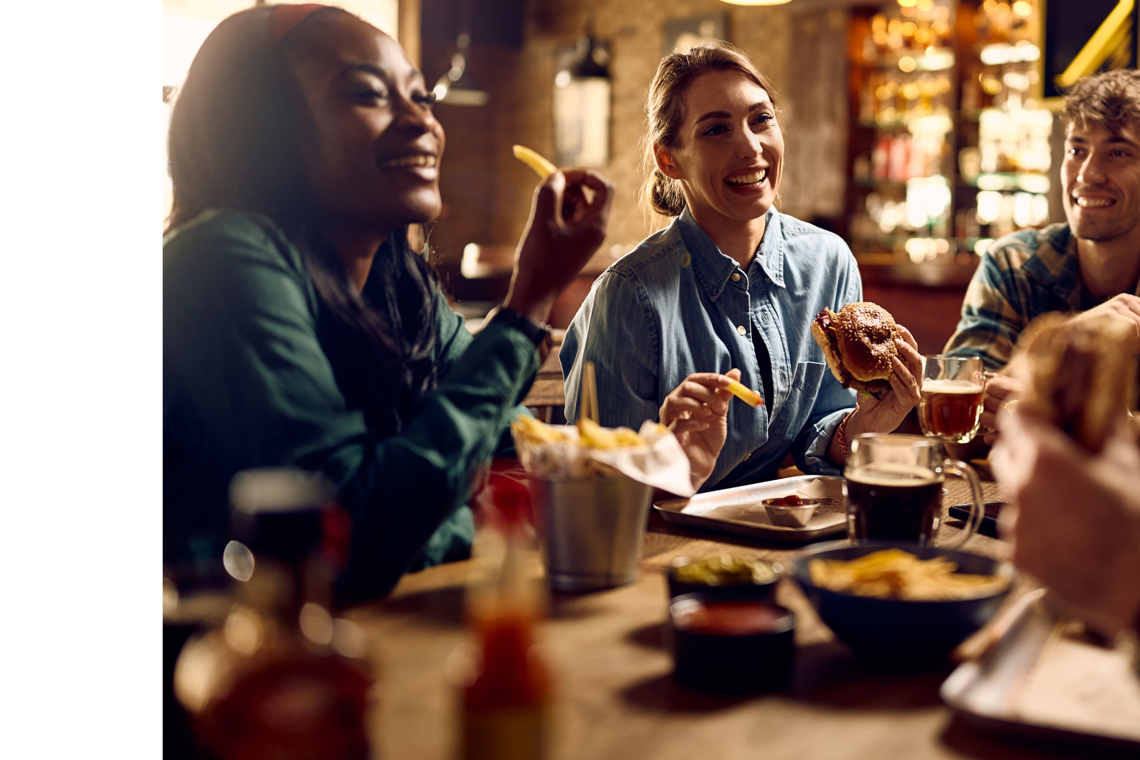 Young happy woman and her friends talking while eating in a pub.