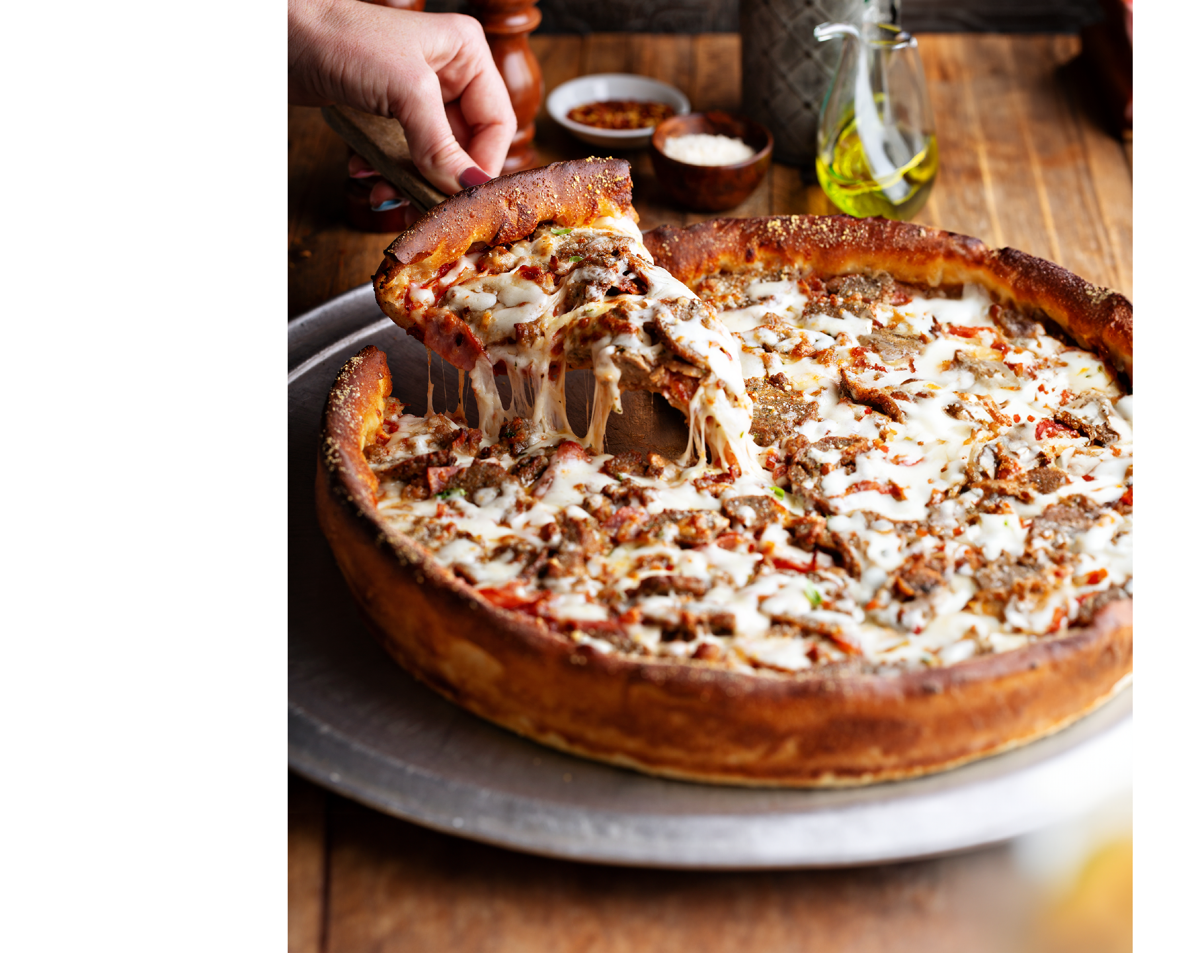 Deep dish meat pizza on a wooden table with a slice being pulled