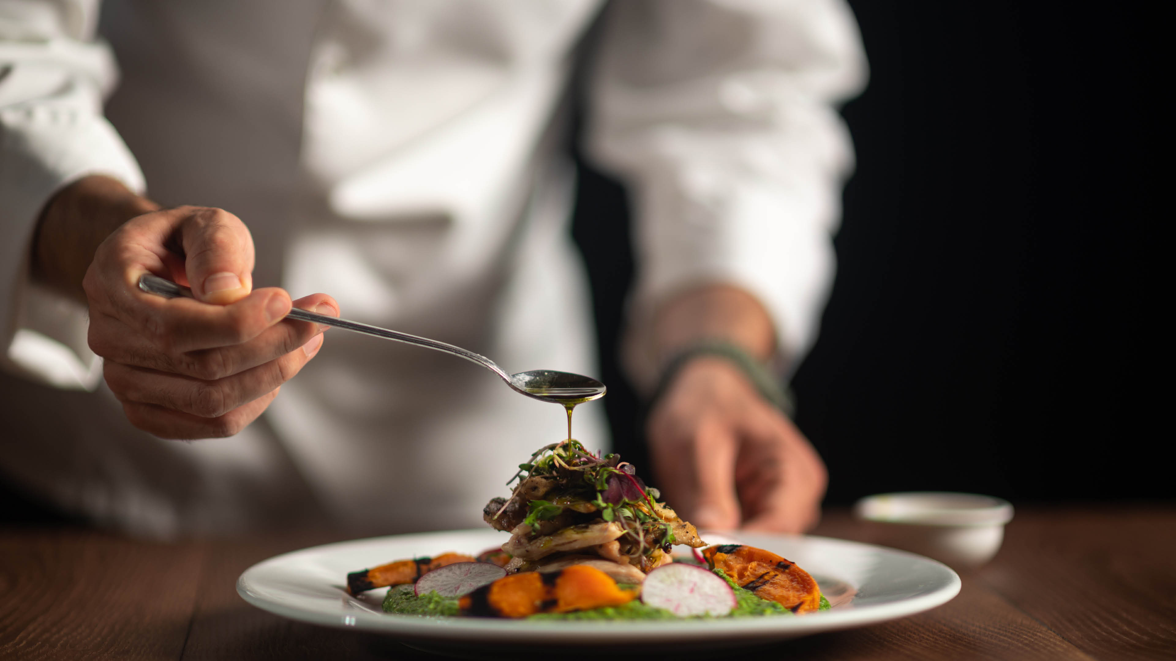 A male chef pouring sauce from the spoon on meal on a black background.
