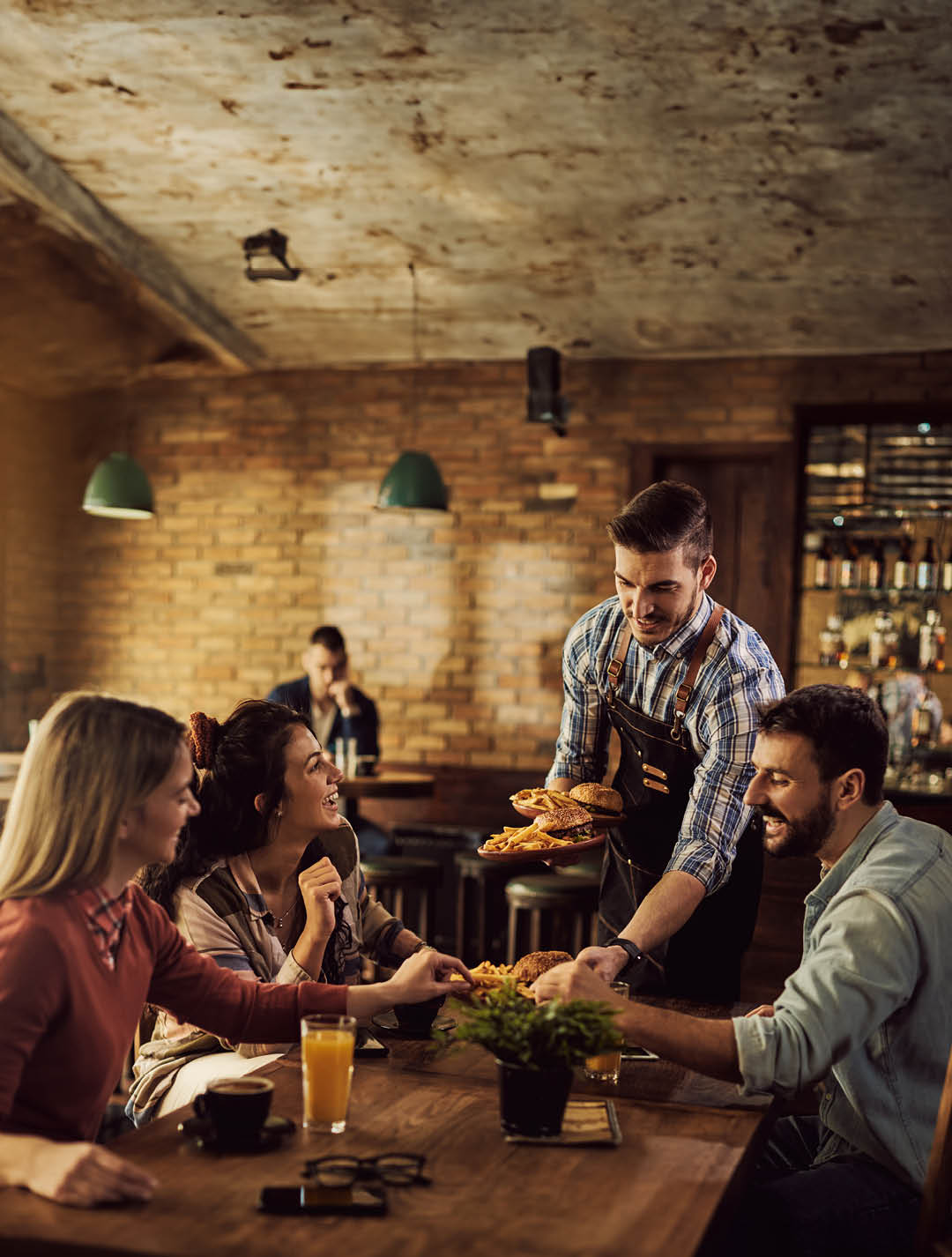 Group of happy friends having fun while waiter is serving them food in a pub.