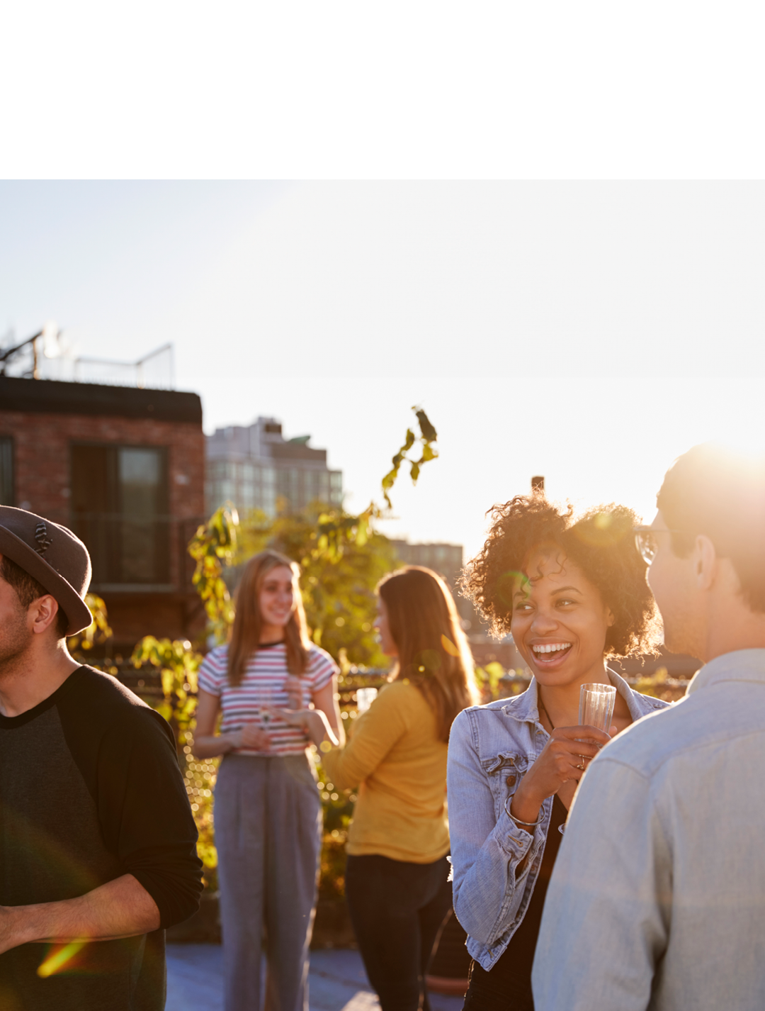 Happy friends at a rooftop party backlit by sunlight
