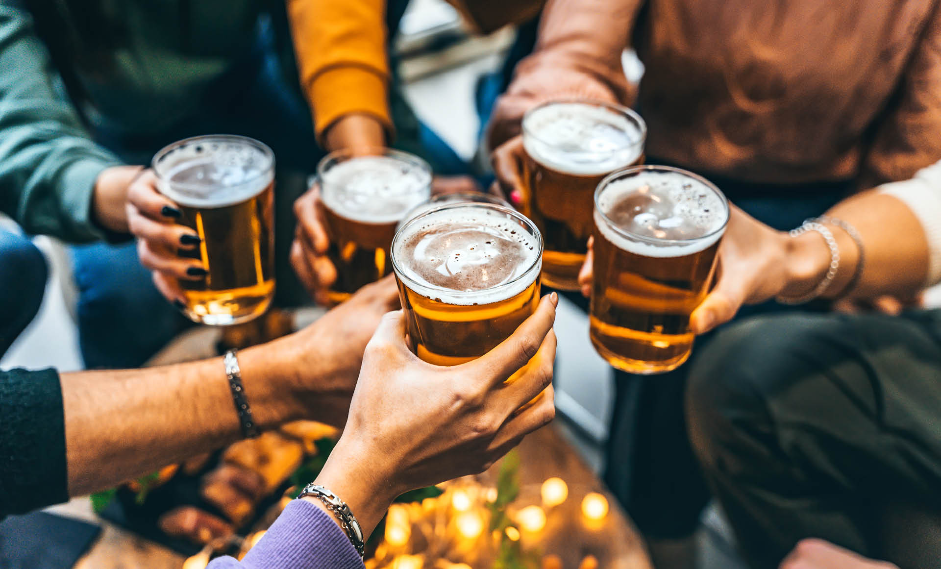 Group of friends drinking and toasting glass of beer at brewery pub restaurant- Happy multiracial people enjoying happy hour with pint sitting at bar table- Youth Food and beverage lifestyle concept