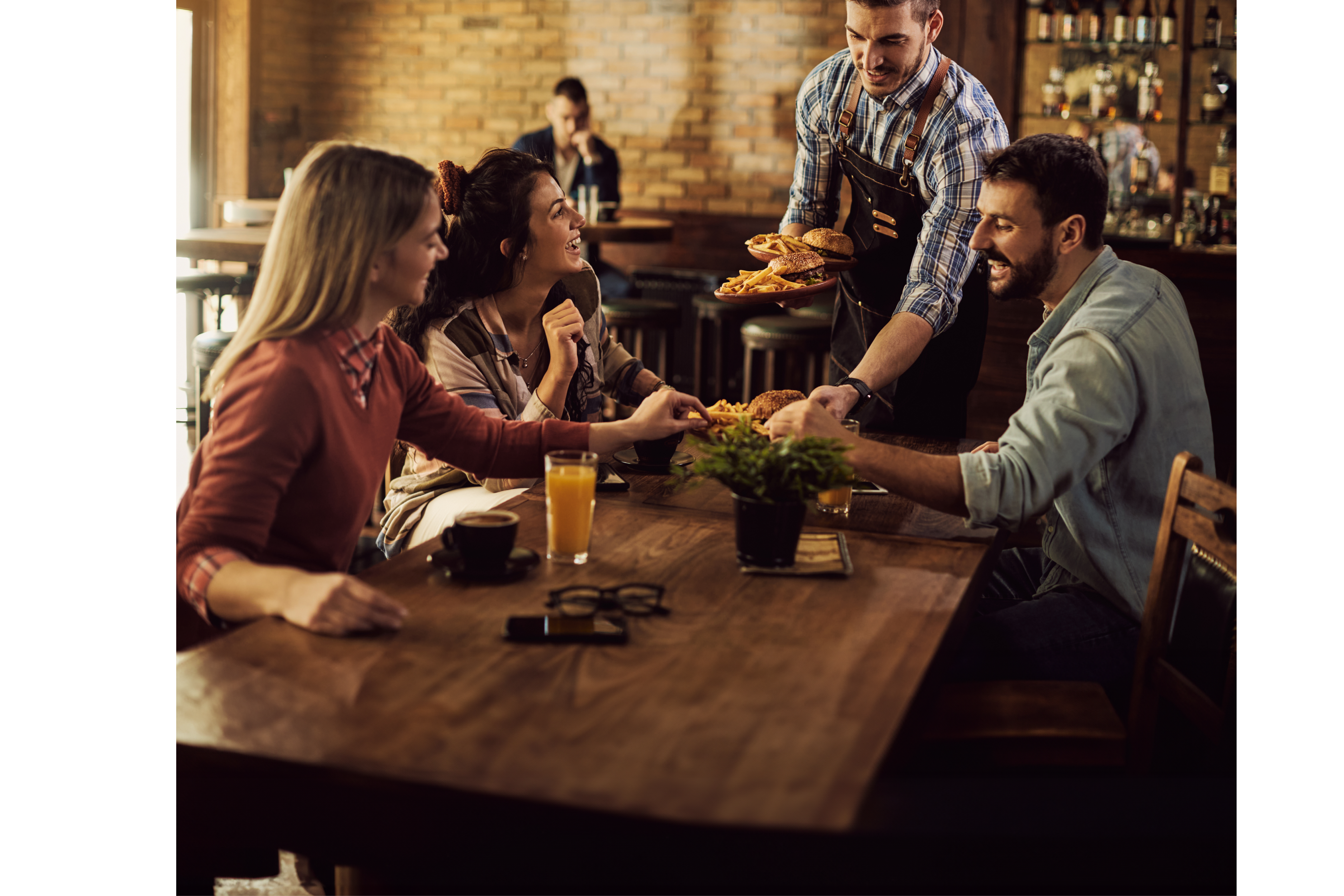 Group of happy friends having fun while waiter is serving them food in a pub.