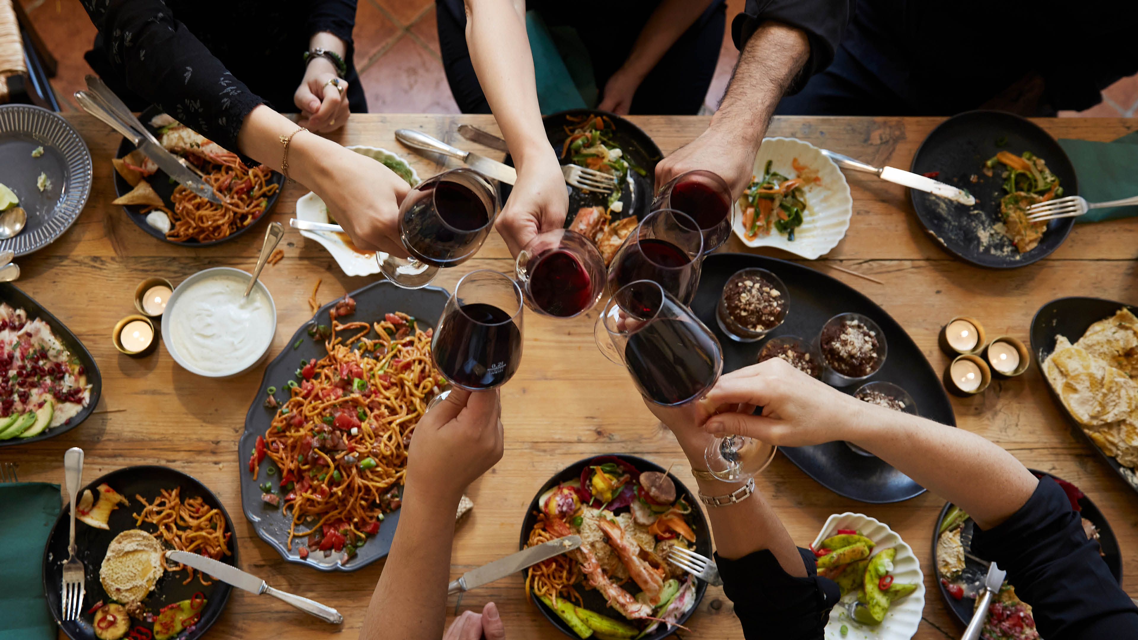 richly set dinner table from above with hands eating drinking and toasting