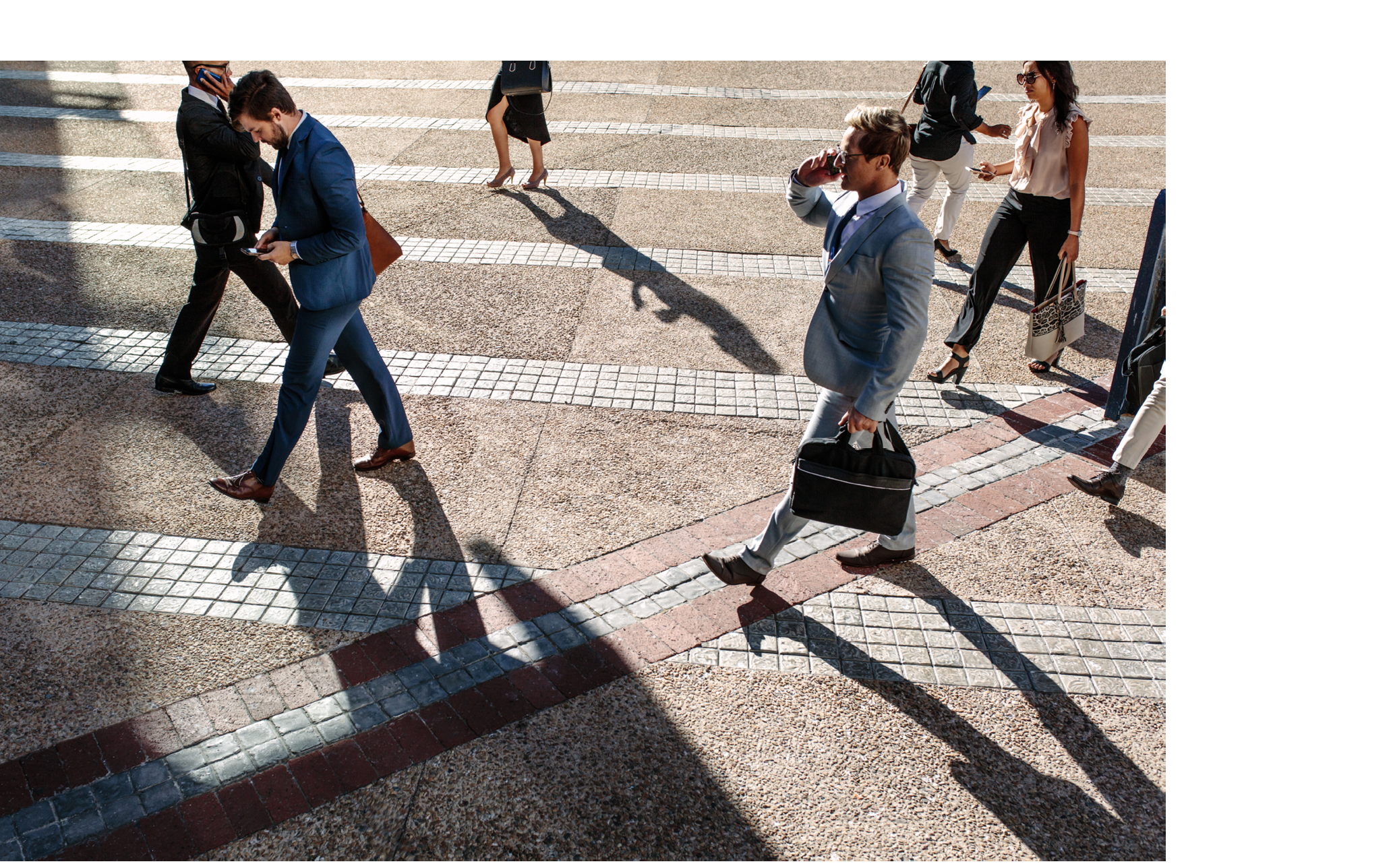 Business people commuting to office in the morning carrying office bags and using mobile phones. Businessmen and businesswomen in a hurry to reach office walking on city street and busy using their mobile phones.