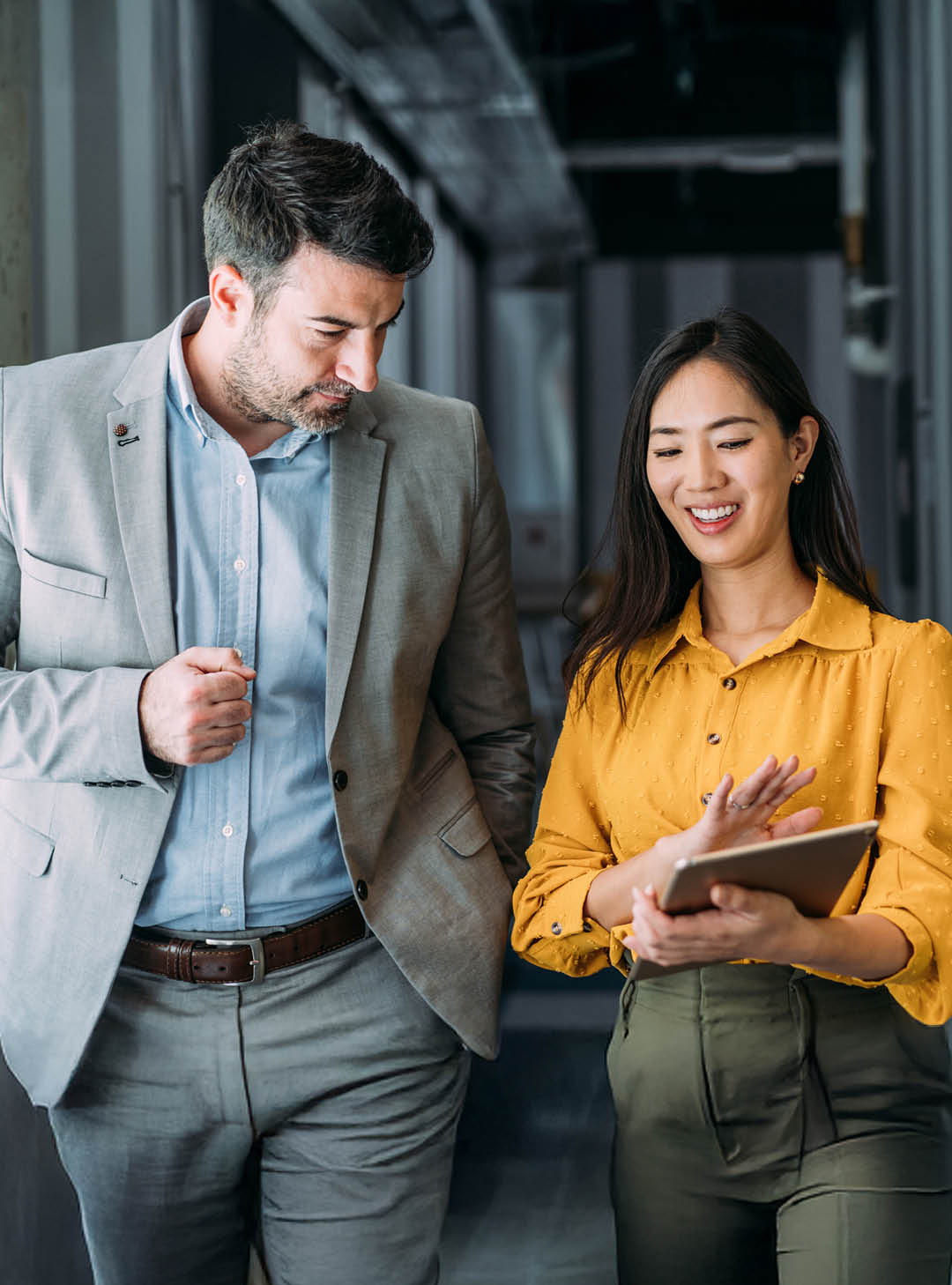 Shot of a two confident business persons talking in the work place. Two colleagues using a digital tablet while walking in a modern office. Businessman and businesswoman in meeting discussing business strategy. Business coworkers working together in the office.