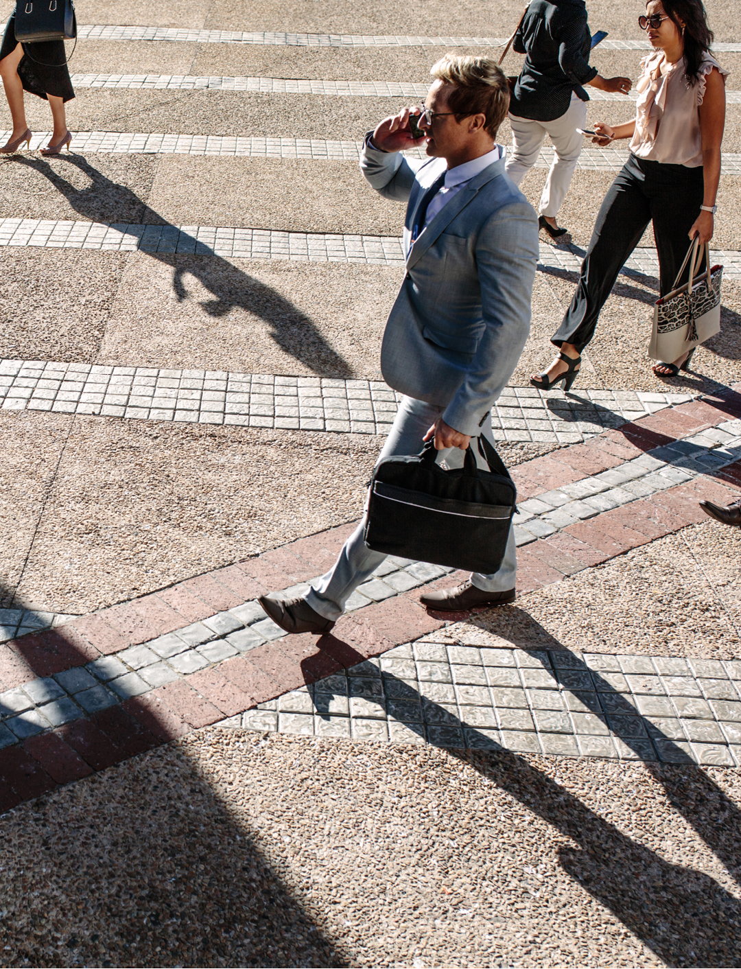Business people commuting to office in the morning carrying office bags and using mobile phones. Businessmen and businesswomen in a hurry to reach office walking on city street and busy using their mobile phones.