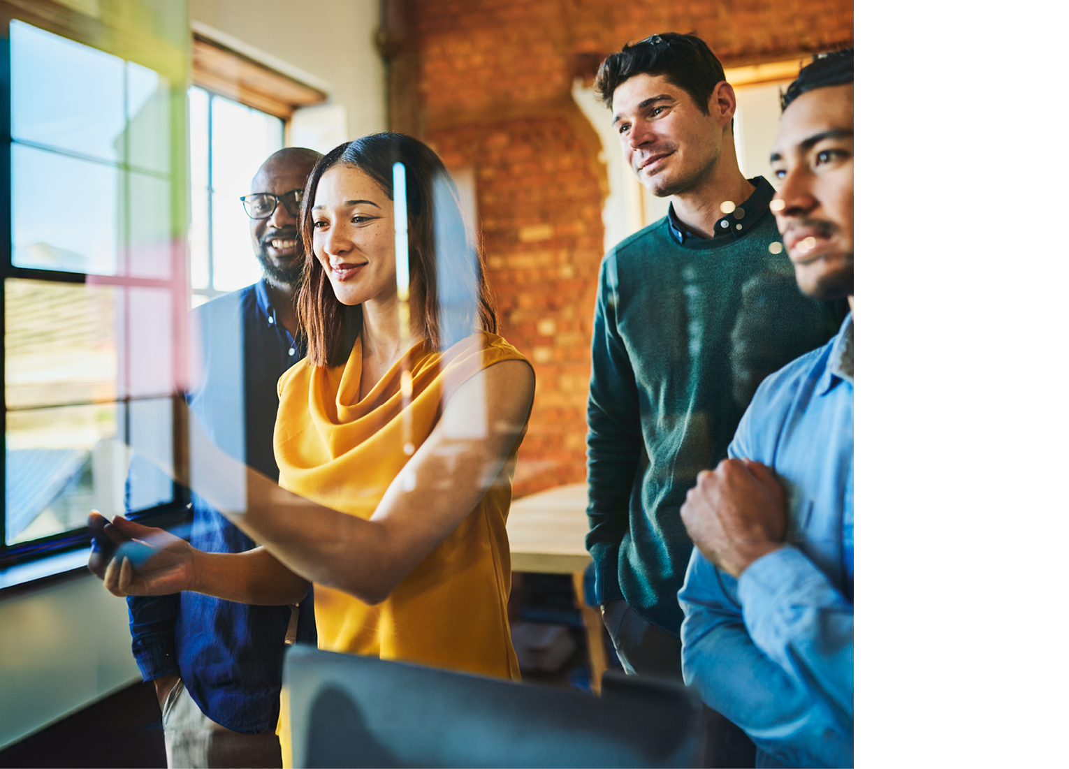 Businesswoman and male colleagues smiling and looking interestingly at sticky notes on glass wall in office