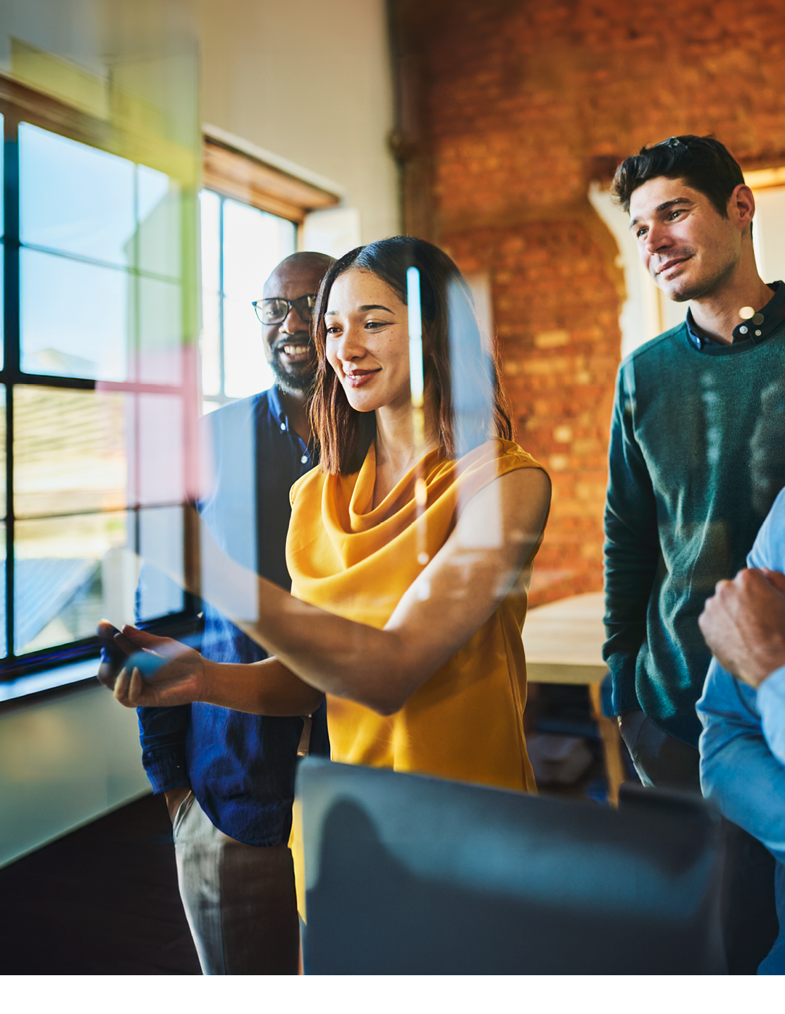 Businesswoman and male colleagues smiling and looking interestingly at sticky notes on glass wall in office