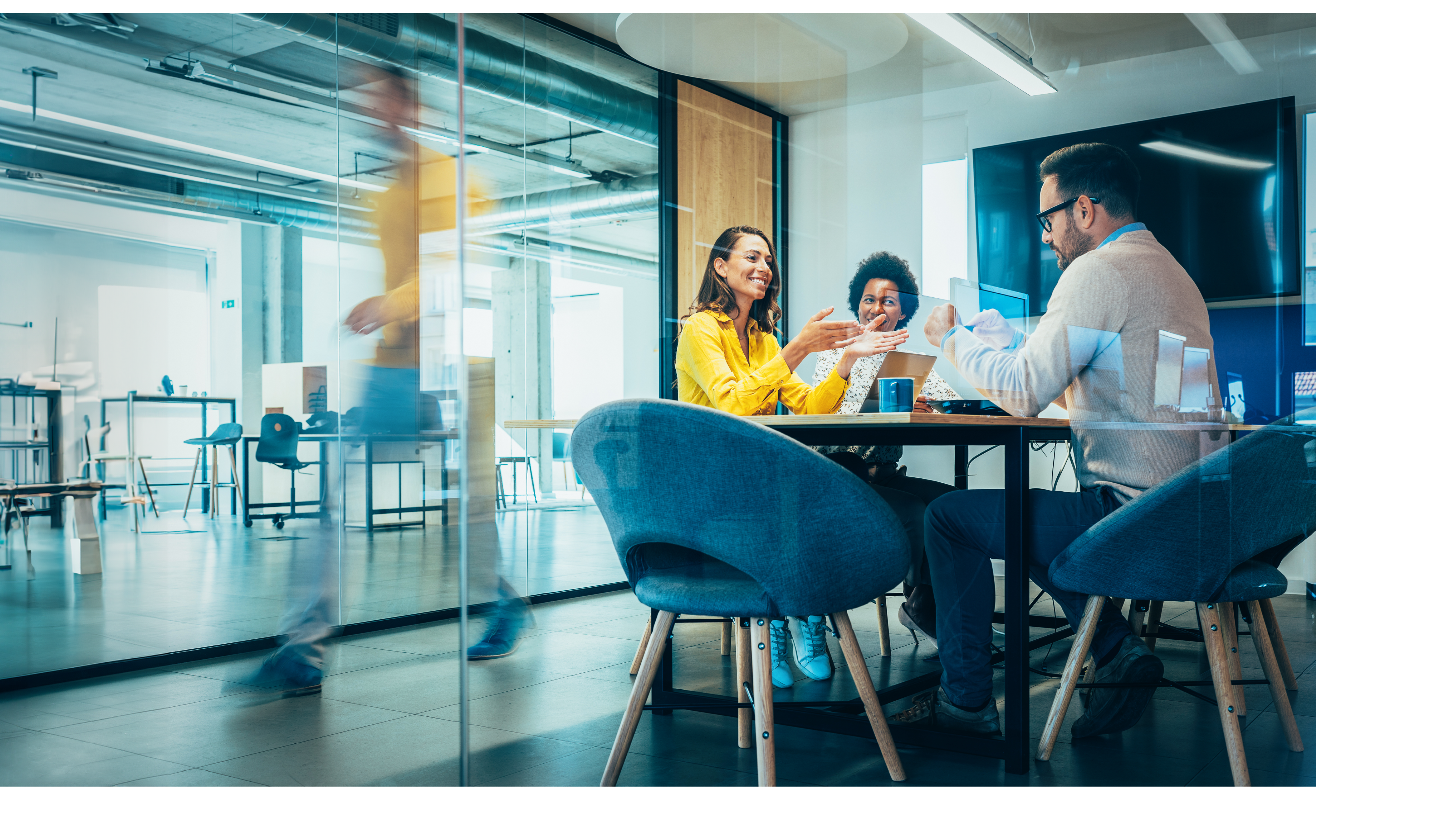 Businesspeople in Conference Room and Colleagues Walking By. Blurred motion of colleagues walking briskly down office hallway as colleagues sit in conference room discussing ideas. Busy modern workplace. Working process in the office, business people working, walking and talking, blurred motion