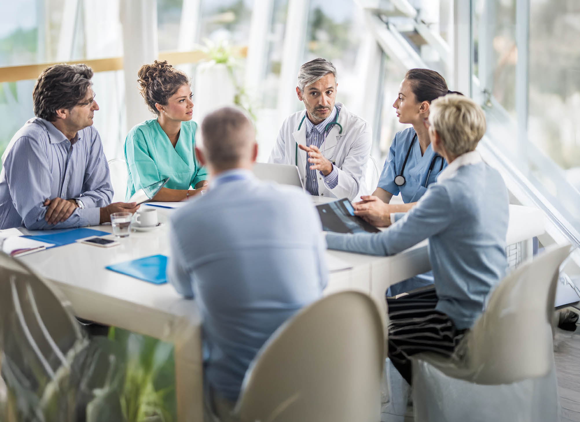 Male doctor and his female colleagues talking to team of business people on a meeting in the hospital.