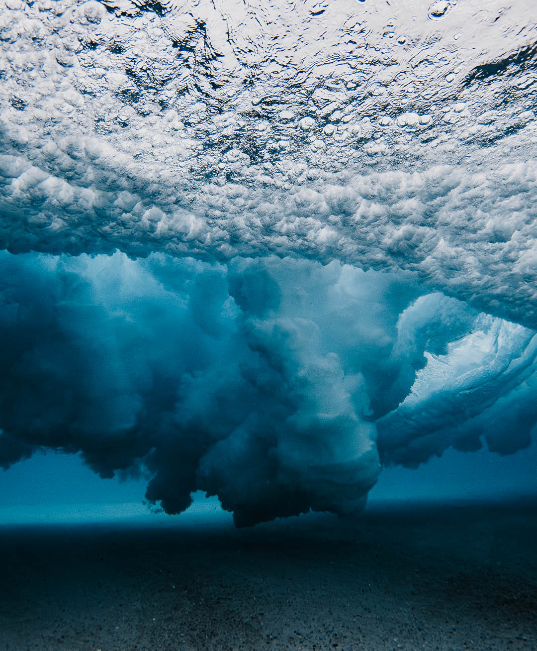 Underwater view beneath a breaking wave exploding with high contrast dispersed water pattern using a flash. Photographed in Western Australia.