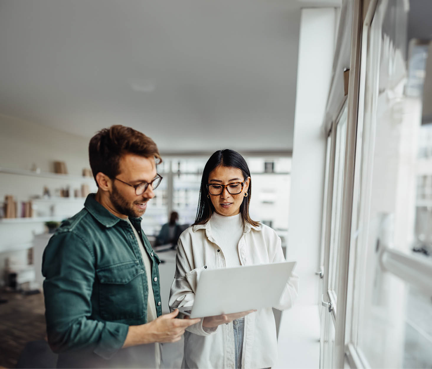 Business professionals standing in an office and using a laptop together. Two young business people having a discussion in a workplace.