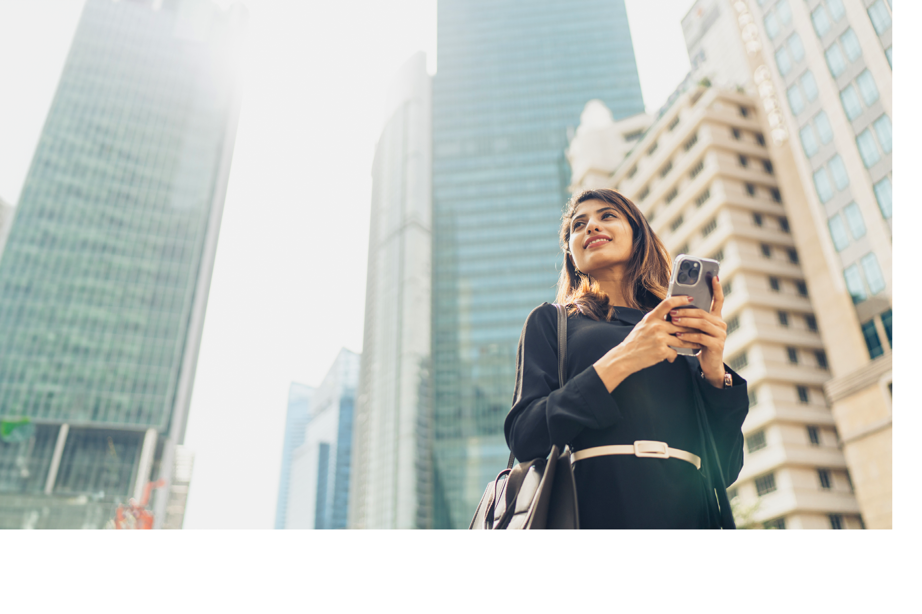 Confident Young Businesswoman With Smartphone Standing Against Modern Buildings