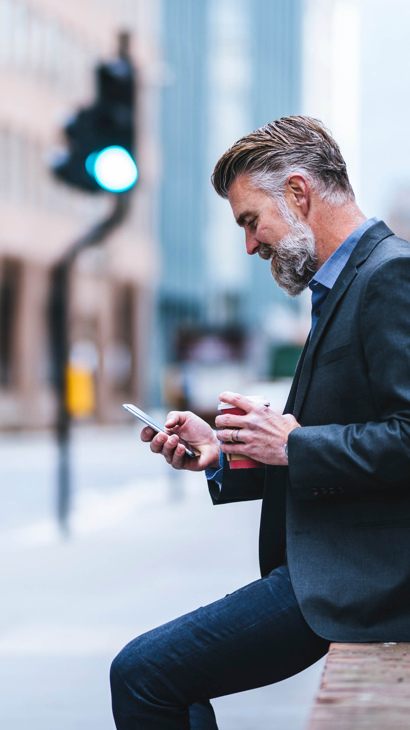 Mid adult businessman on the go. He is using mobile phone and holding coffee cup. Double-decker bus in the back.