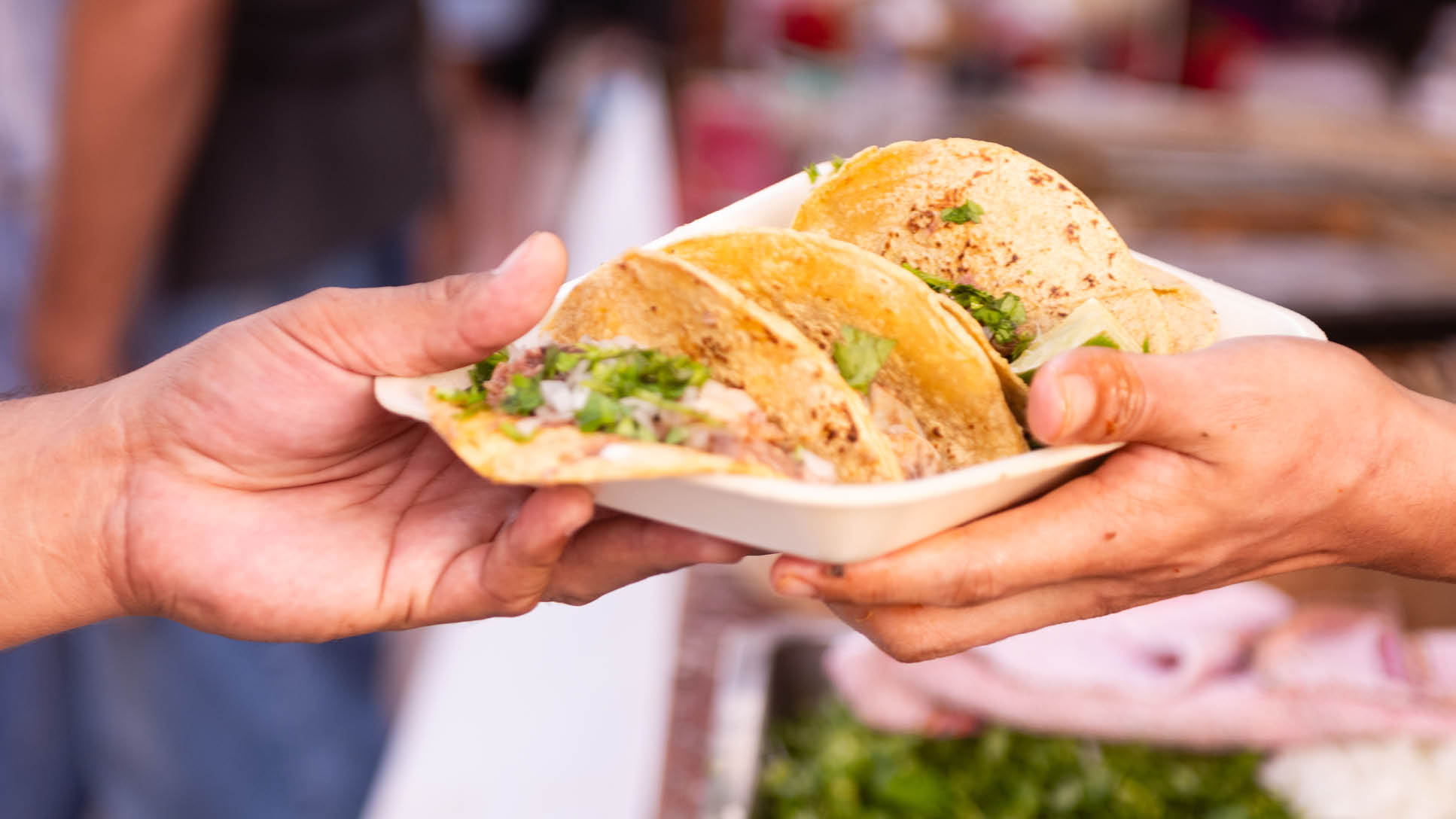 During the Dia de los Muertos holiday celebrations the hands of an unrecognizable person hands a plate of tacos to a customer outdoors in Playa del Carmen, Mexico.