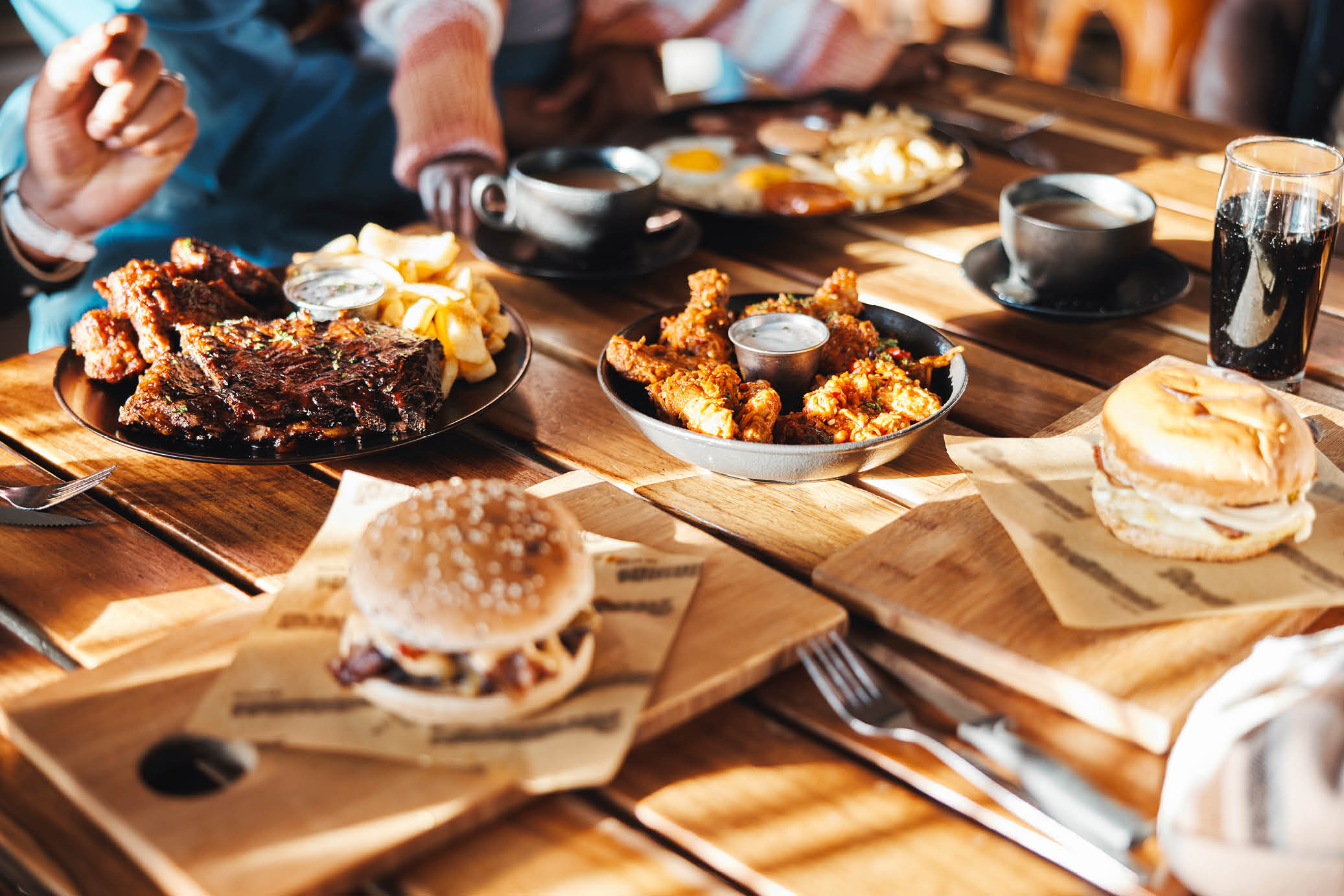 Fast food, lunch or dinner on table at restaurant, people eating for nutrition and wellness with time together. Catering, hospitality and cuisine with burger, chicken and ribs for protein at diner