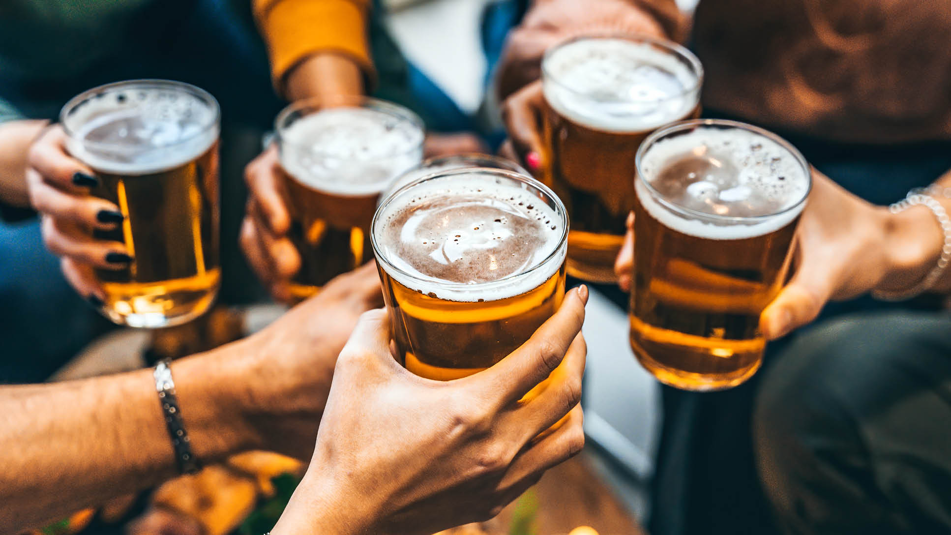 Group of friends drinking and toasting glass of beer at brewery pub restaurant- Happy multiracial people enjoying happy hour with pint sitting at bar table- Youth Food and beverage lifestyle concept