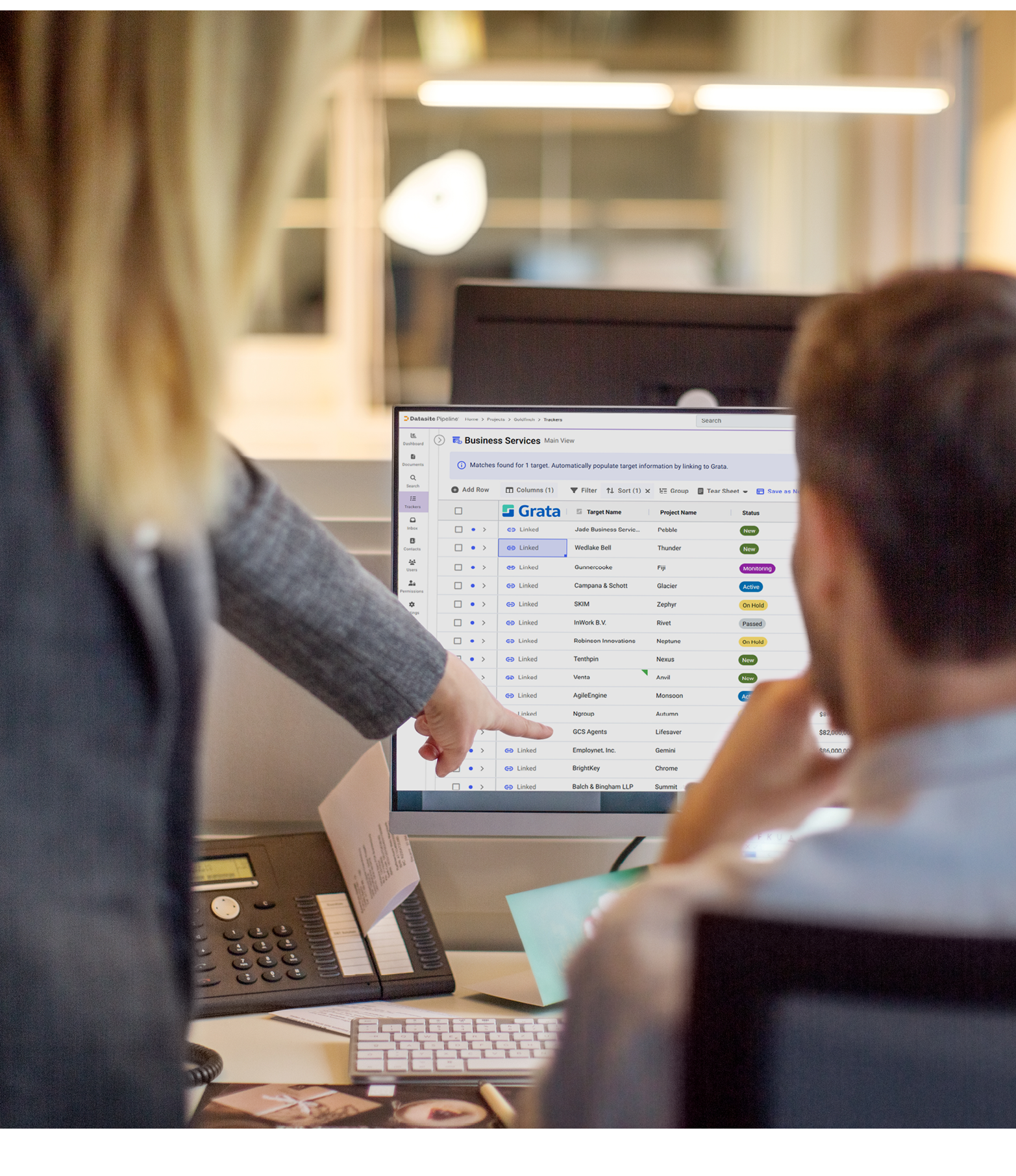 Rear view of two business people working together on computer. Woman pointing at computer monitor with man sitting by in office.