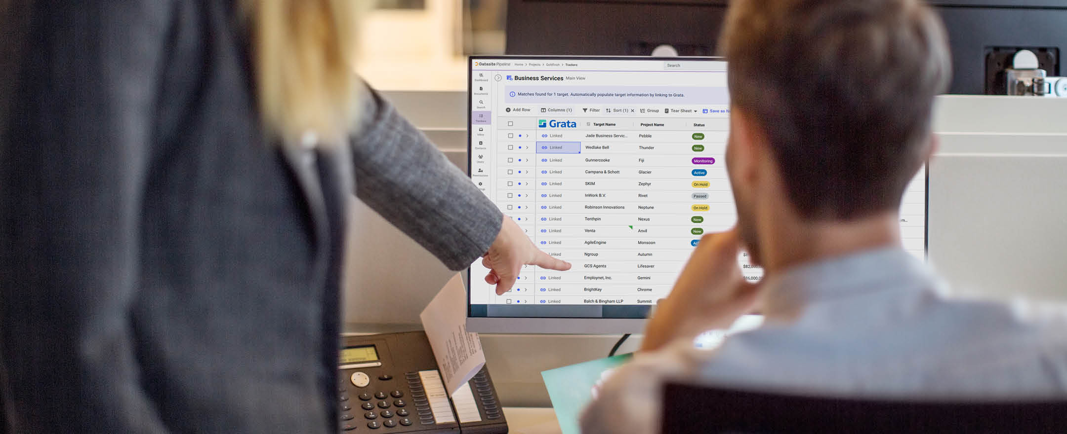 Rear view of two business people working together on computer. Woman pointing at computer monitor with man sitting by in office.